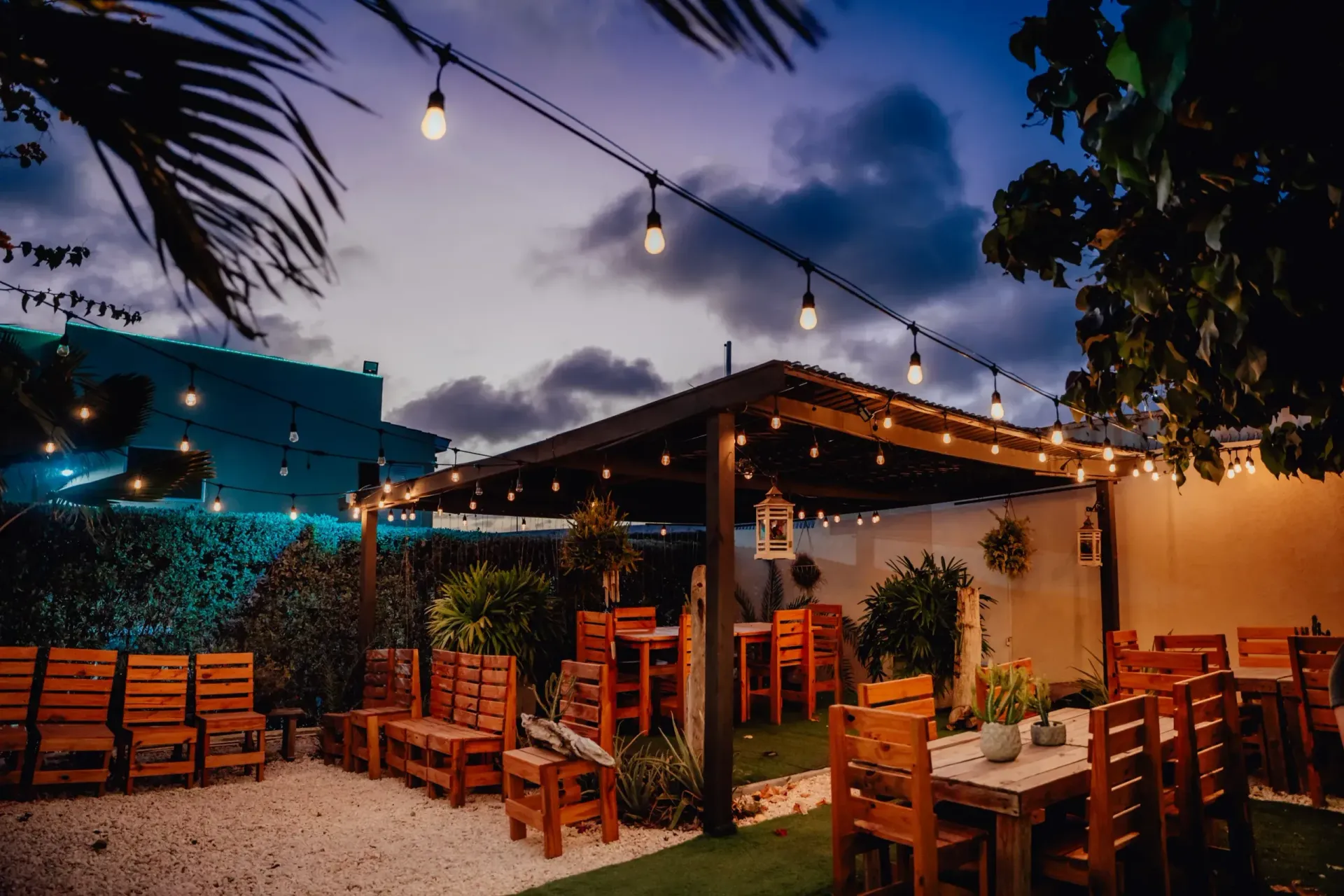 A patio with tables and chairs under a pergola at night.
