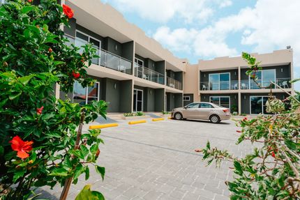 Modern motel courtyard with parked car, balconies, and green shrubs under a blue sky