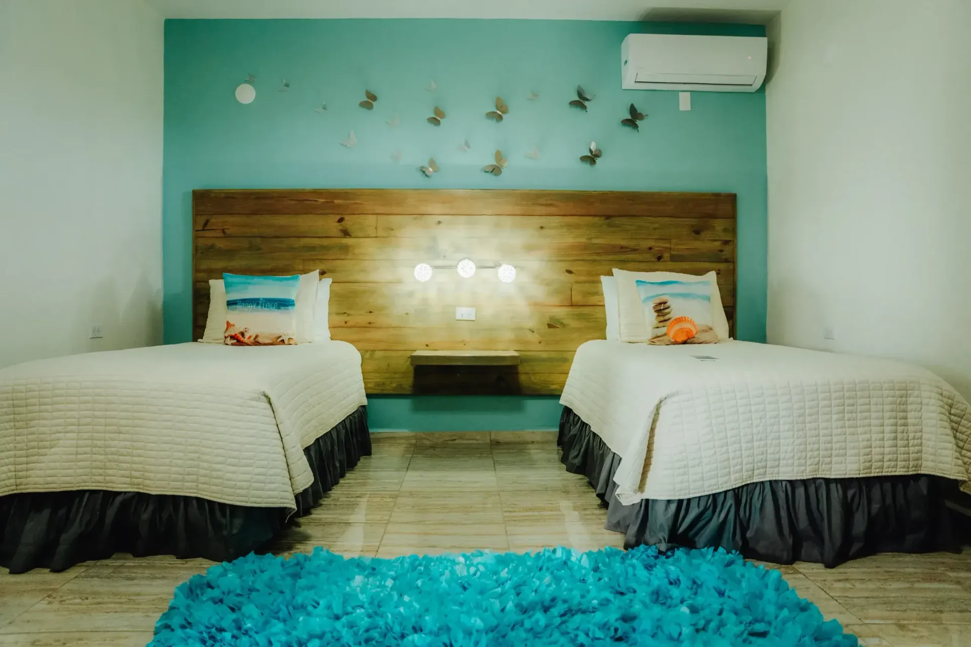 Twin beds in a turquoise bedroom with a wood headboard, wall birds, and a blue rug.
