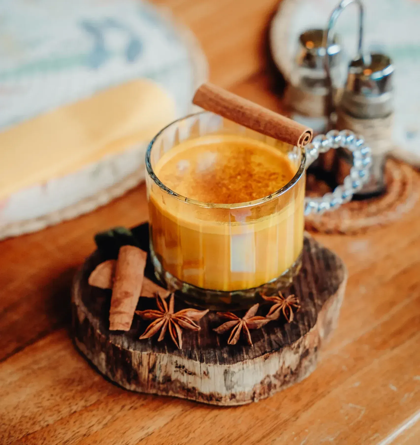 A cup of golden milk with cinnamon sticks and star anise on a wooden table.
