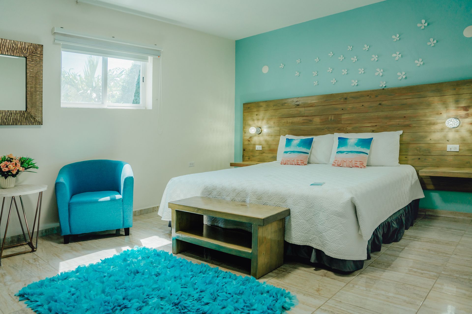Bright turquoise bedroom with a bed, blue chair, window, and teal rug