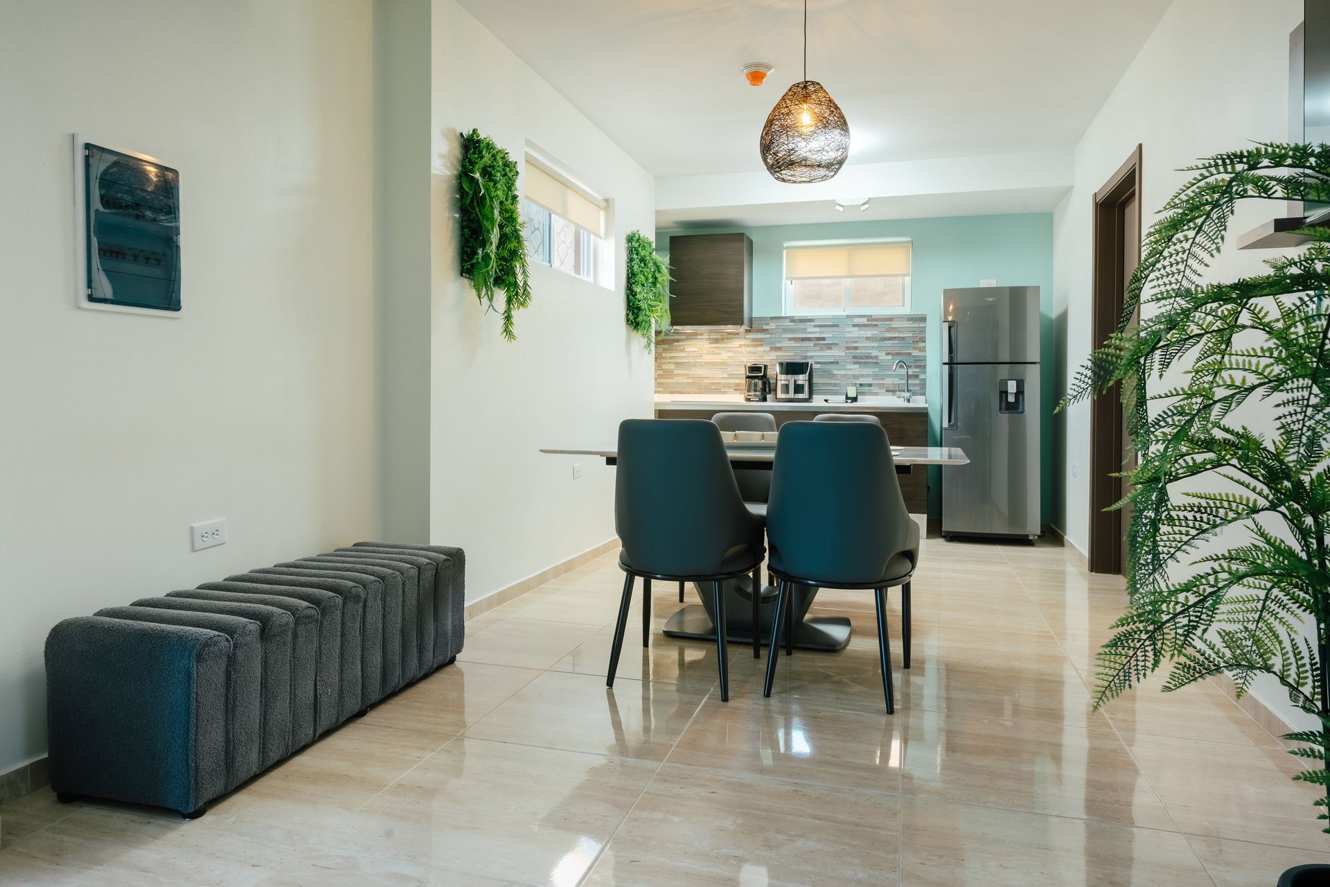 Modern dining area with teal chairs, marble floor, kitchen view, and indoor plants