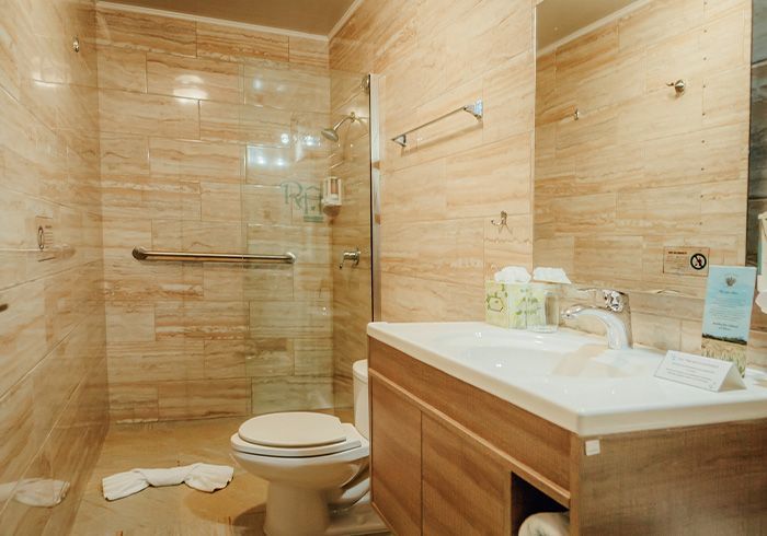 Modern beige bathroom with glass shower, toilet, and wooden vanity sink