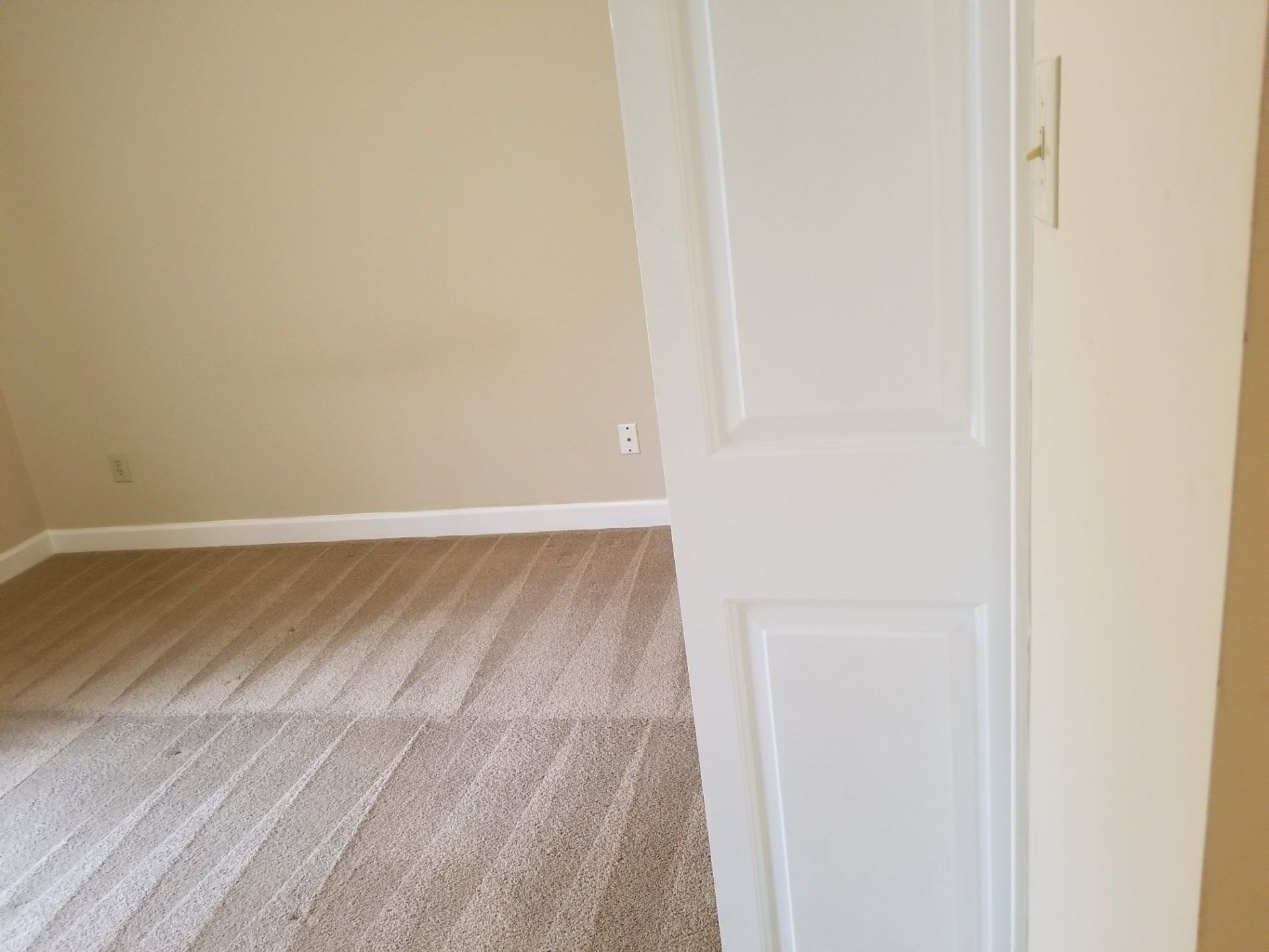 Carpet cleaning service in Durham, NC, empty beige room with striped carpet and a partially open white door