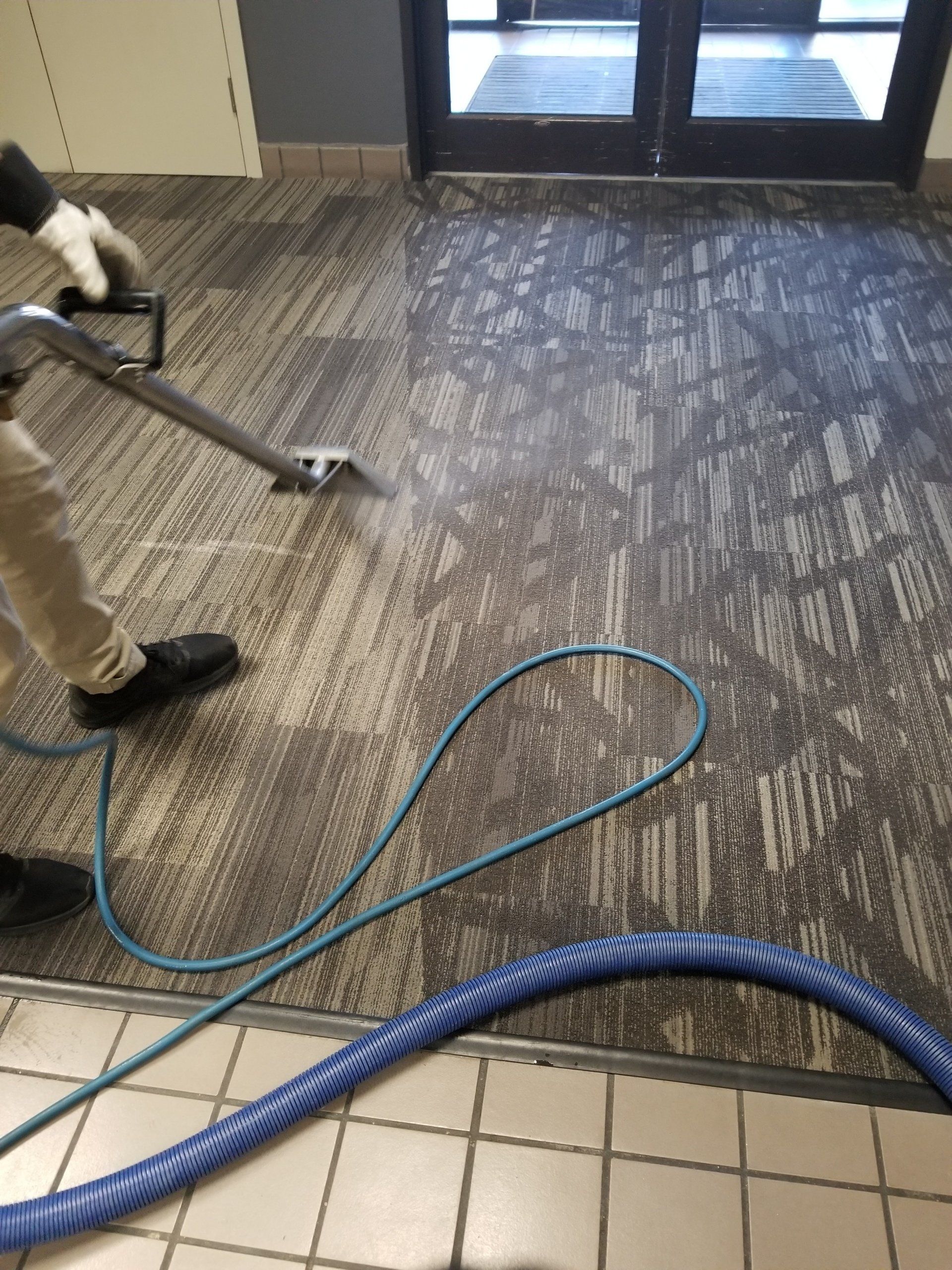 Carpet cleaning in Durham, NC, worker using pressure washer in lobby near glass entrance with hoses on floor.