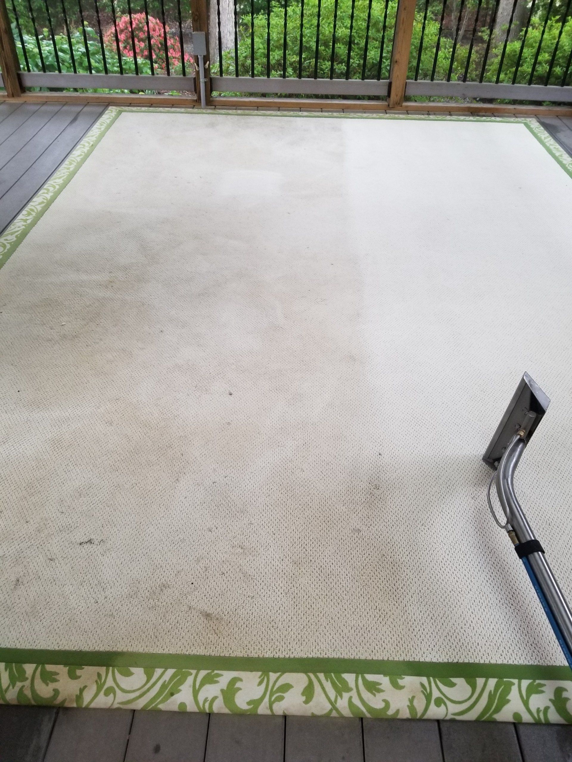 Rug and upholstery cleaning in Durham, NC, carpet cleaner nozzle over light rug with green border near patio.