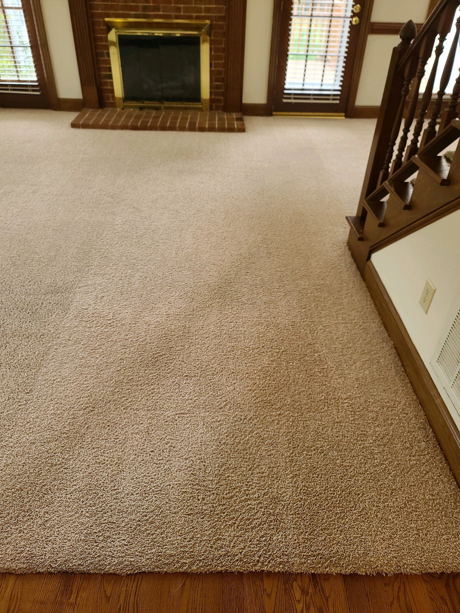 Carpet cleaning in Durham, NC, carpeted living room with a fireplace and staircase railing, viewed from the top of the stairs