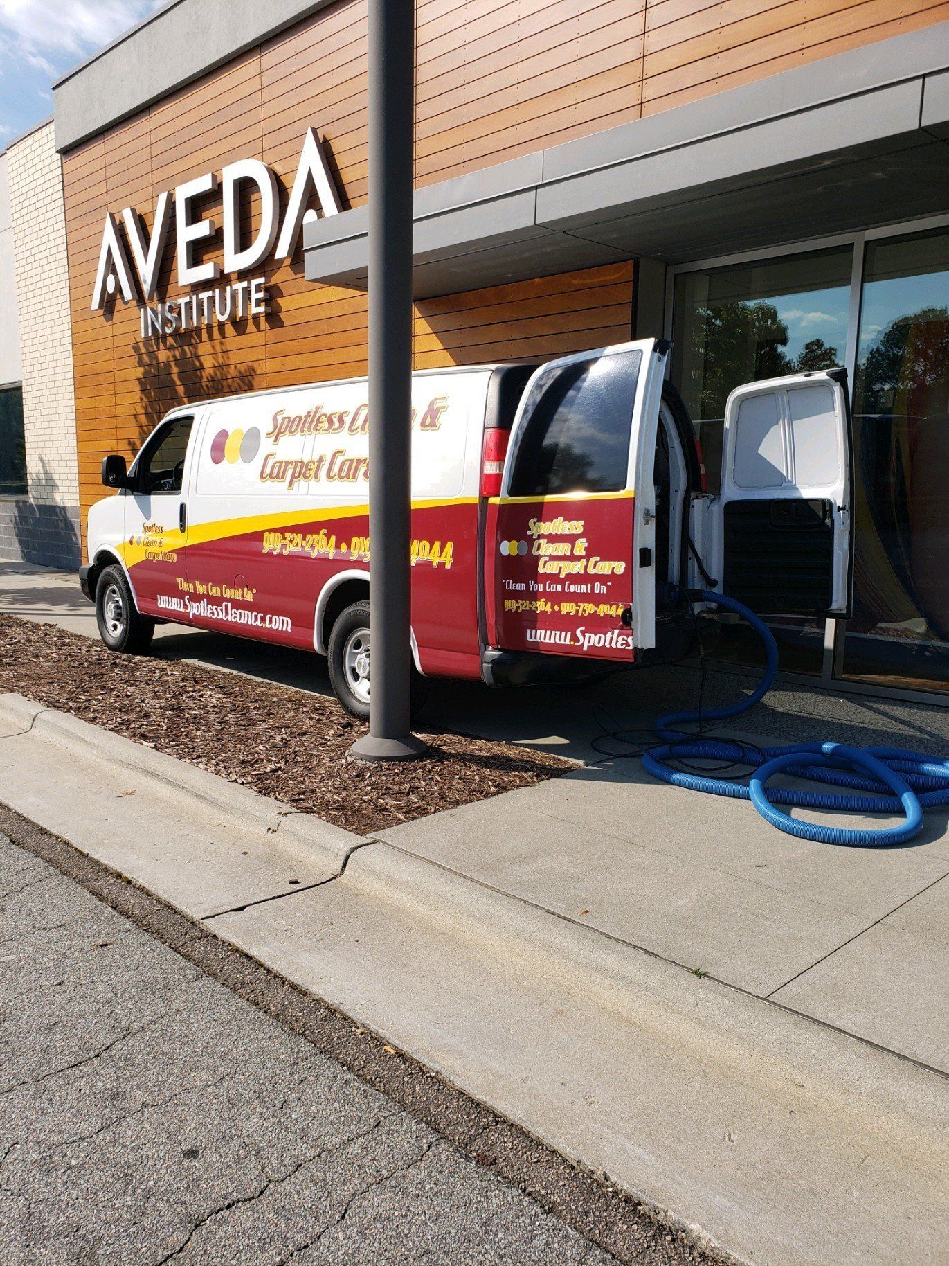 Carpet cleaning in Durham, NC, service van parked by AVEDA Institute with open doors and hoses on sidewalk.