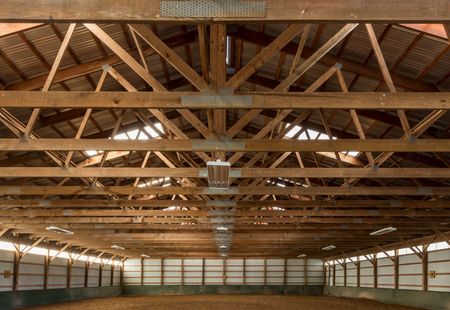 Empty wooden barn interior with exposed roof trusses and a dirt floor