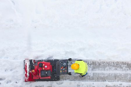 Person in a yellow jacket operating a red snowblower on a snowy path, top-down view