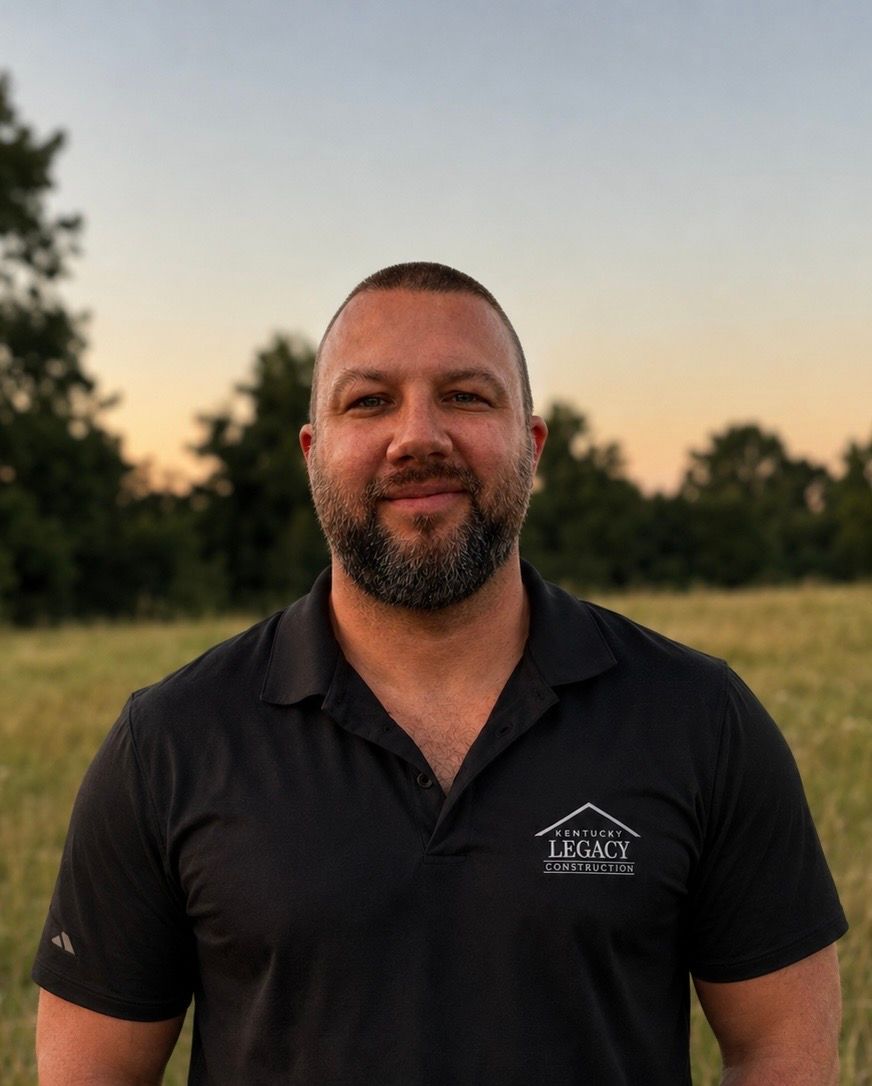 Man in a black polo shirt standing outdoors at sunset with trees in the background