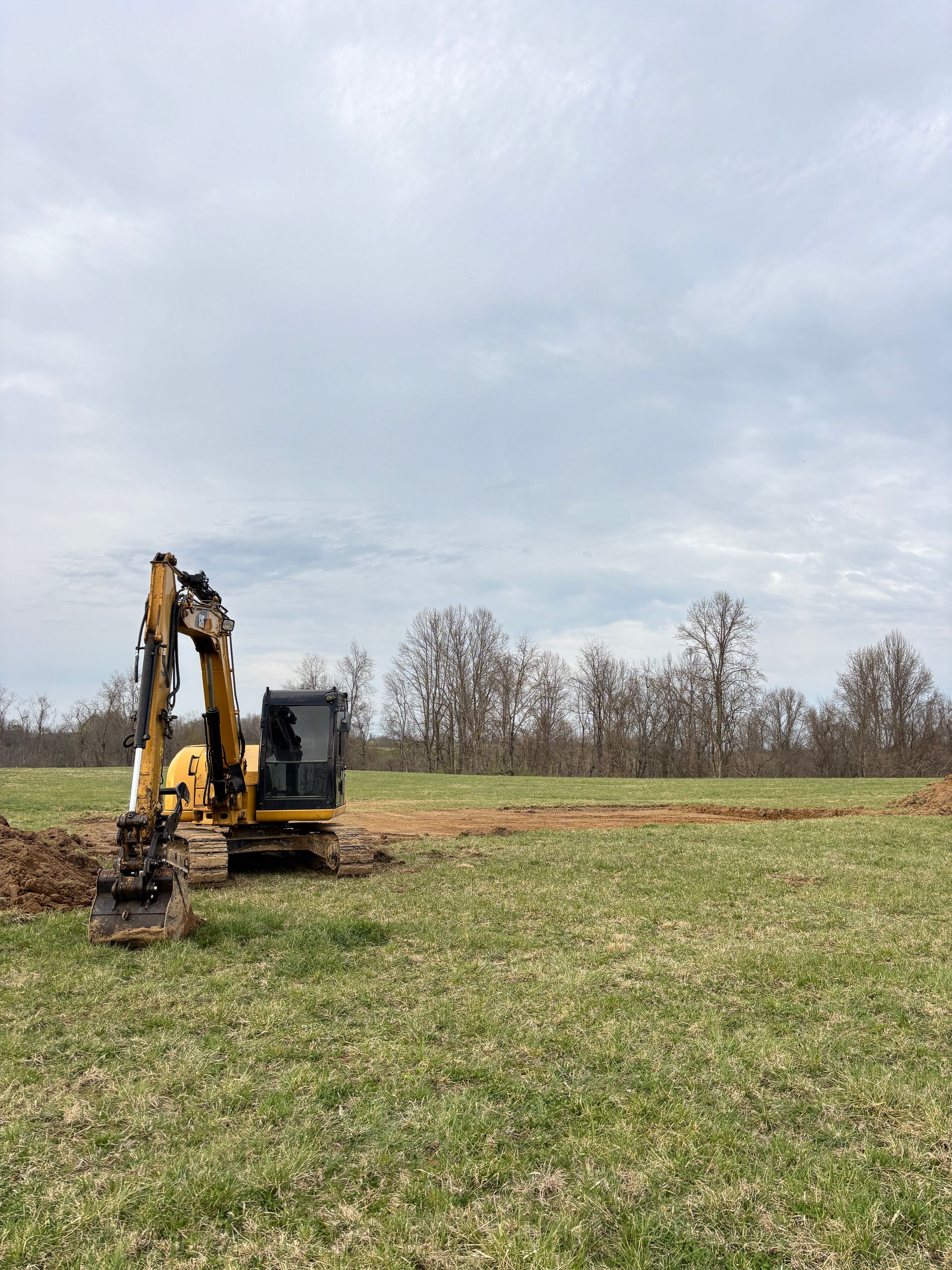 Yellow excavator in a grassy field under a cloudy sky