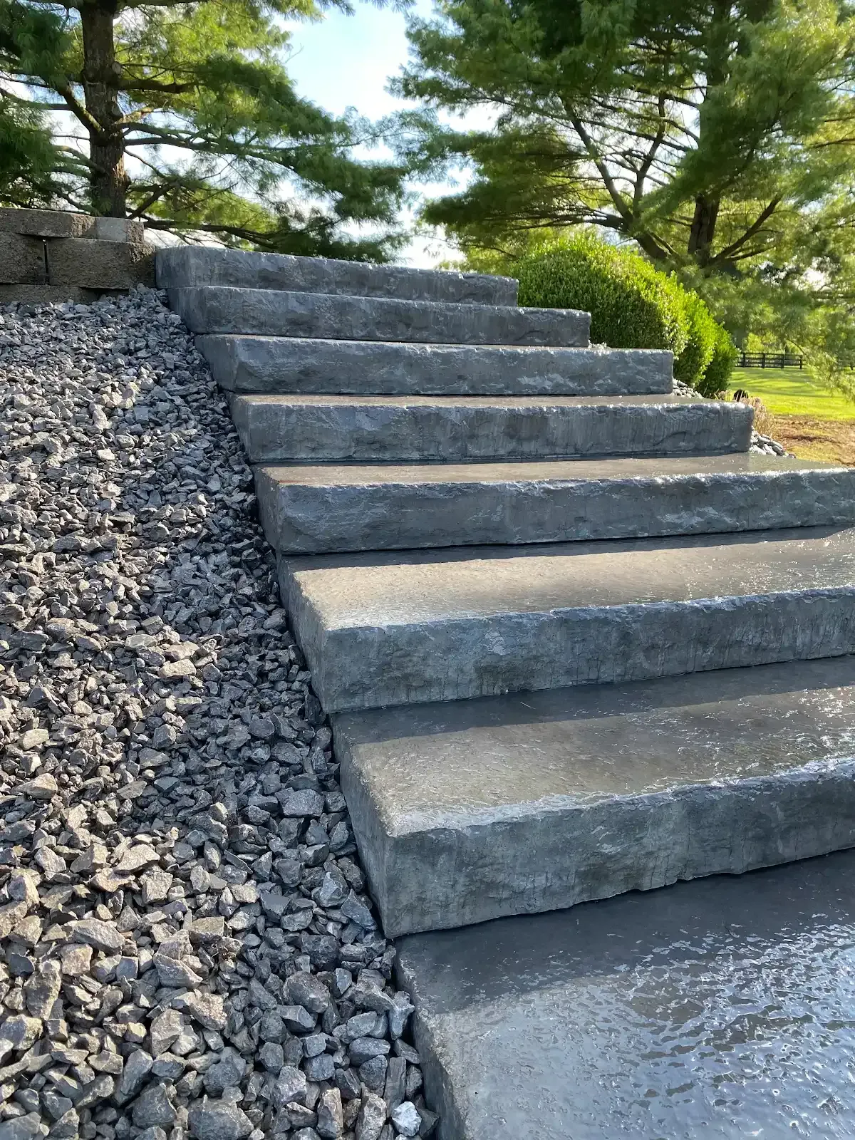 Concrete outdoor steps beside a gravel slope and green trees in a landscaped garden