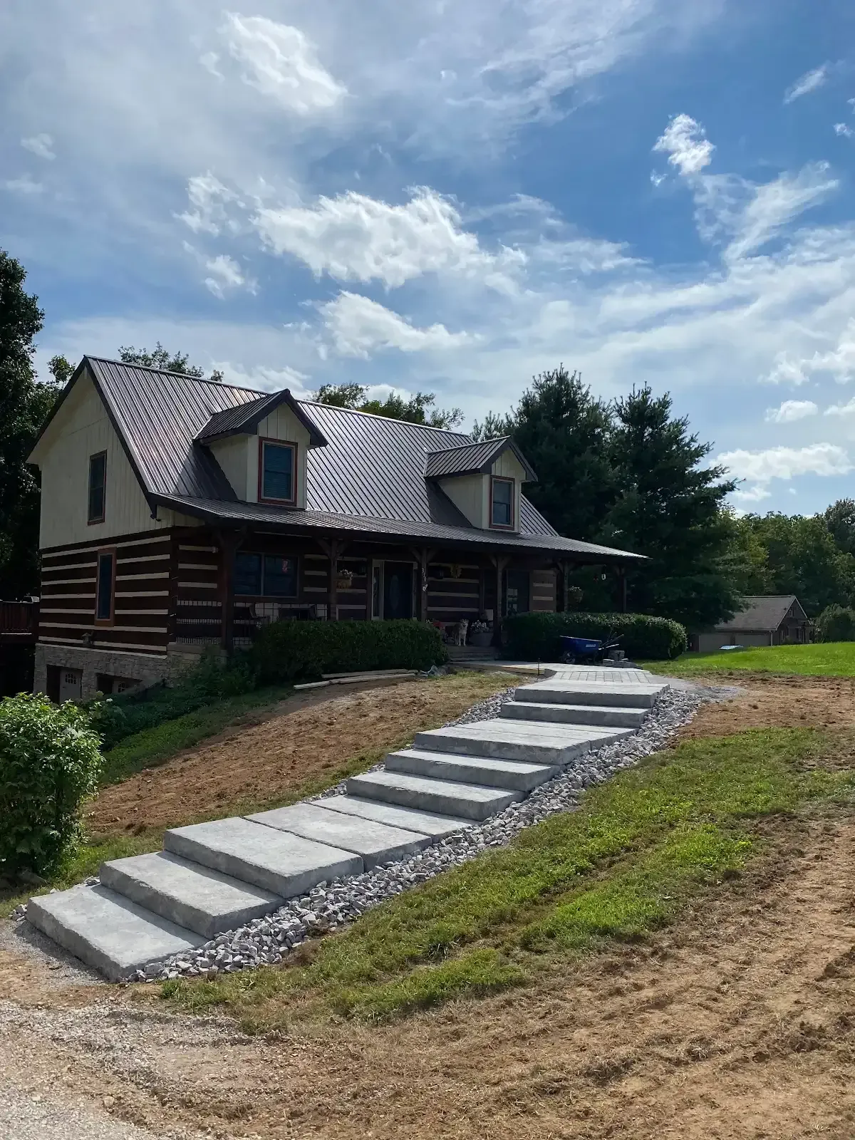 Log cabin with steep concrete steps on a grassy hillside under a partly cloudy sky