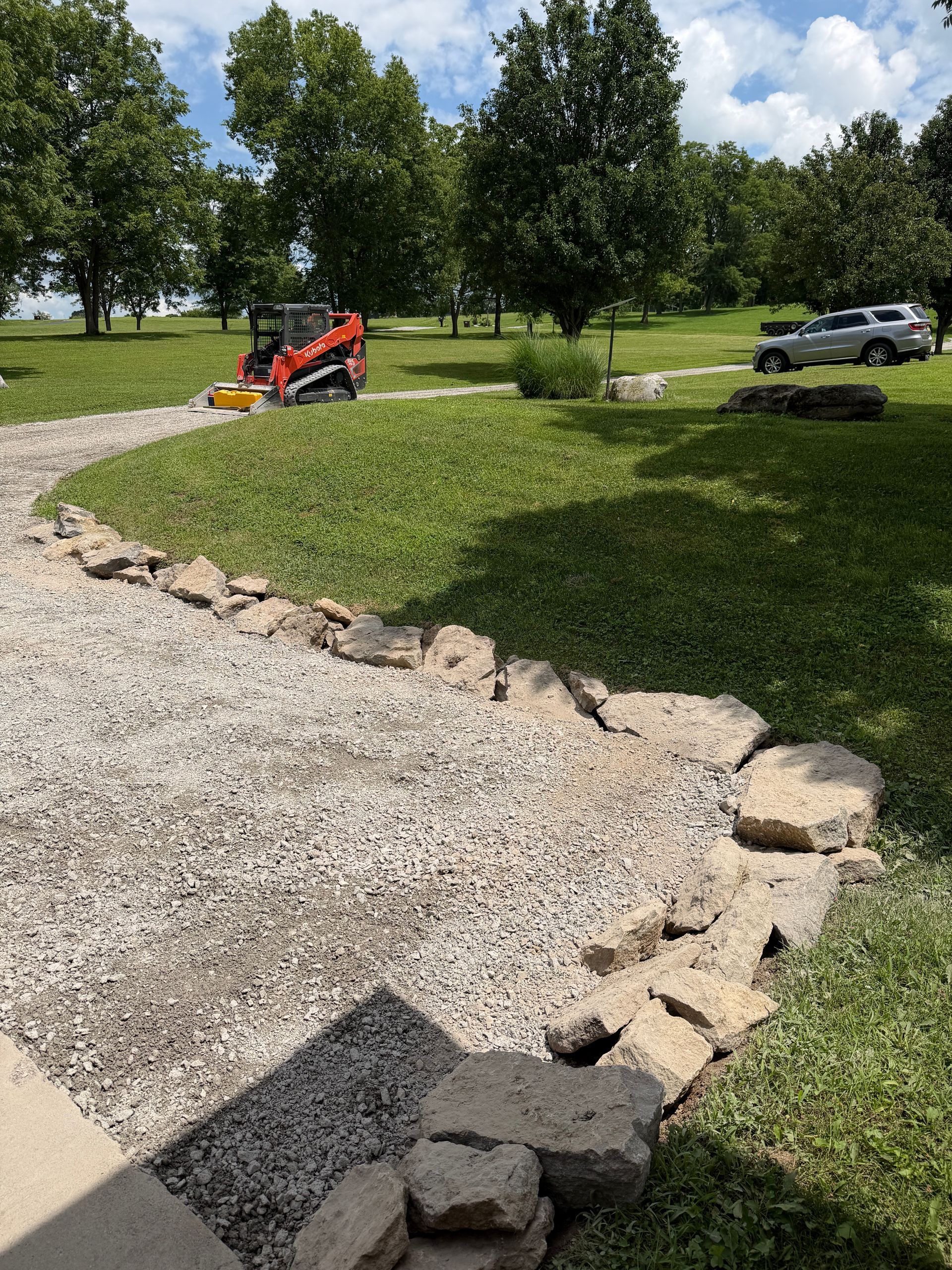 Gravel path beside a grassy slope with rocks, a red tractor, and a white pickup in a sunny park