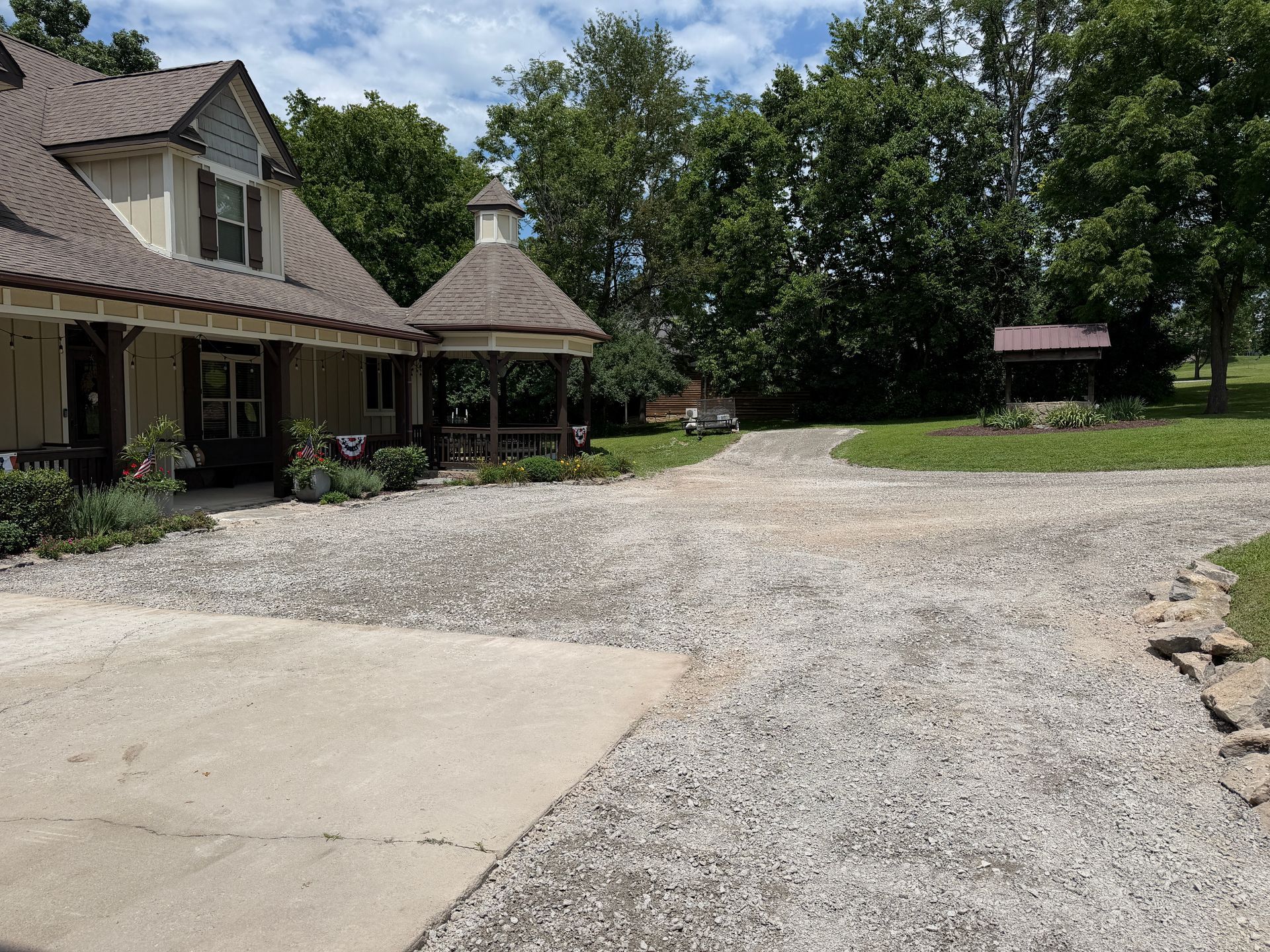 Large house with a gravel driveway and trees in a sunny rural setting