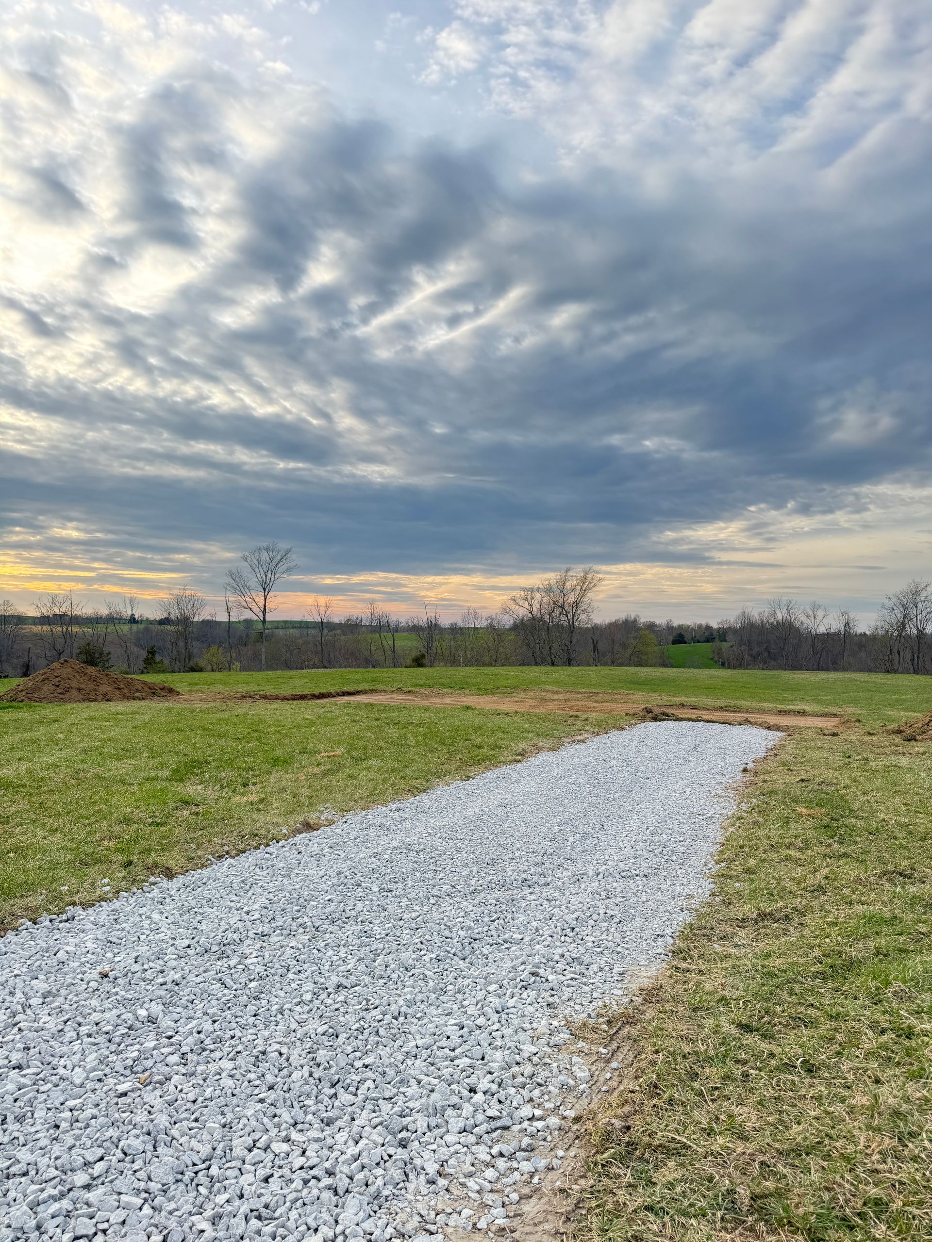 Gravel path through grassy field under a cloudy sunset sky