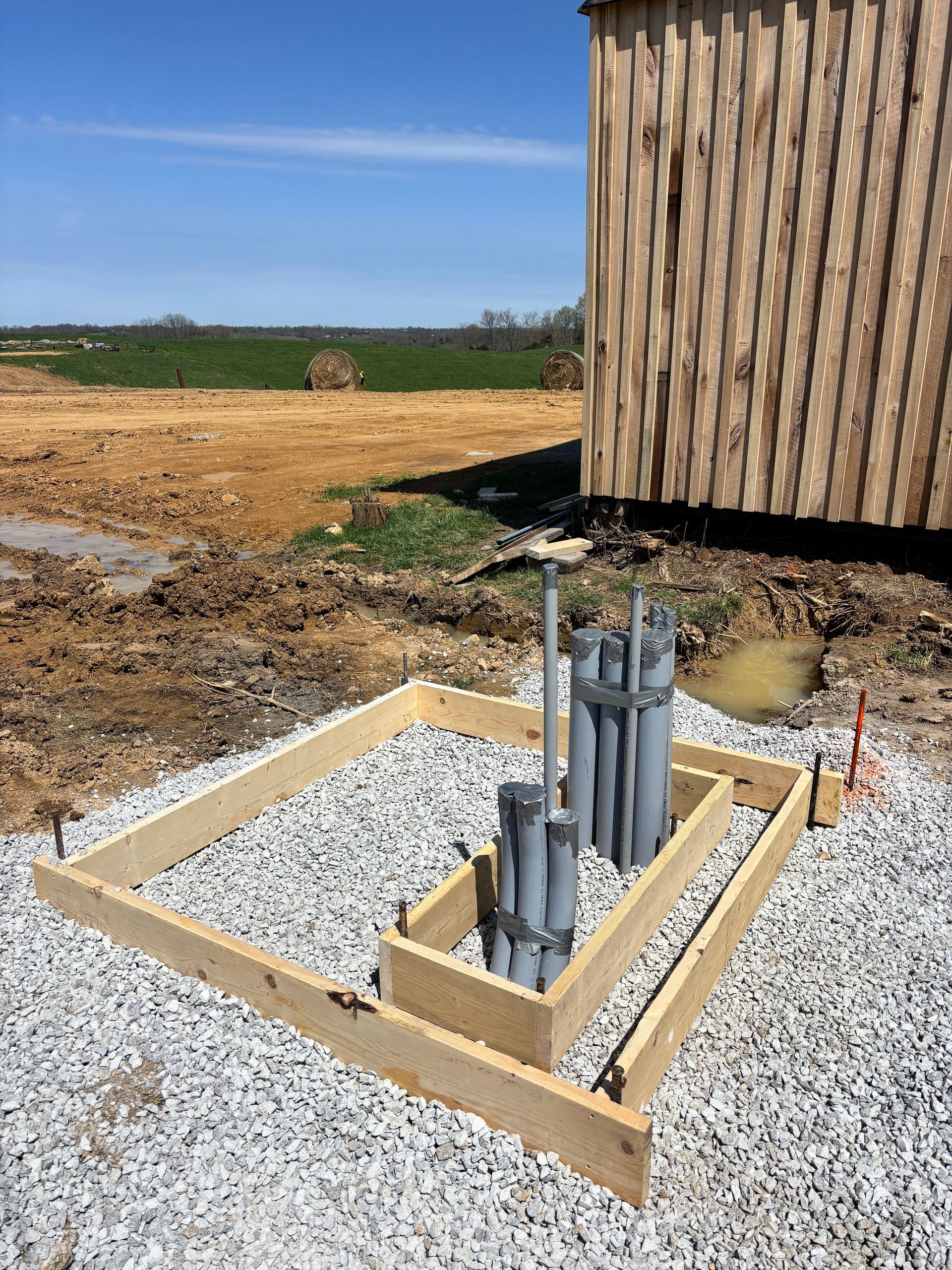 Utility piping in a gravel foundation beside a wooden building under construction