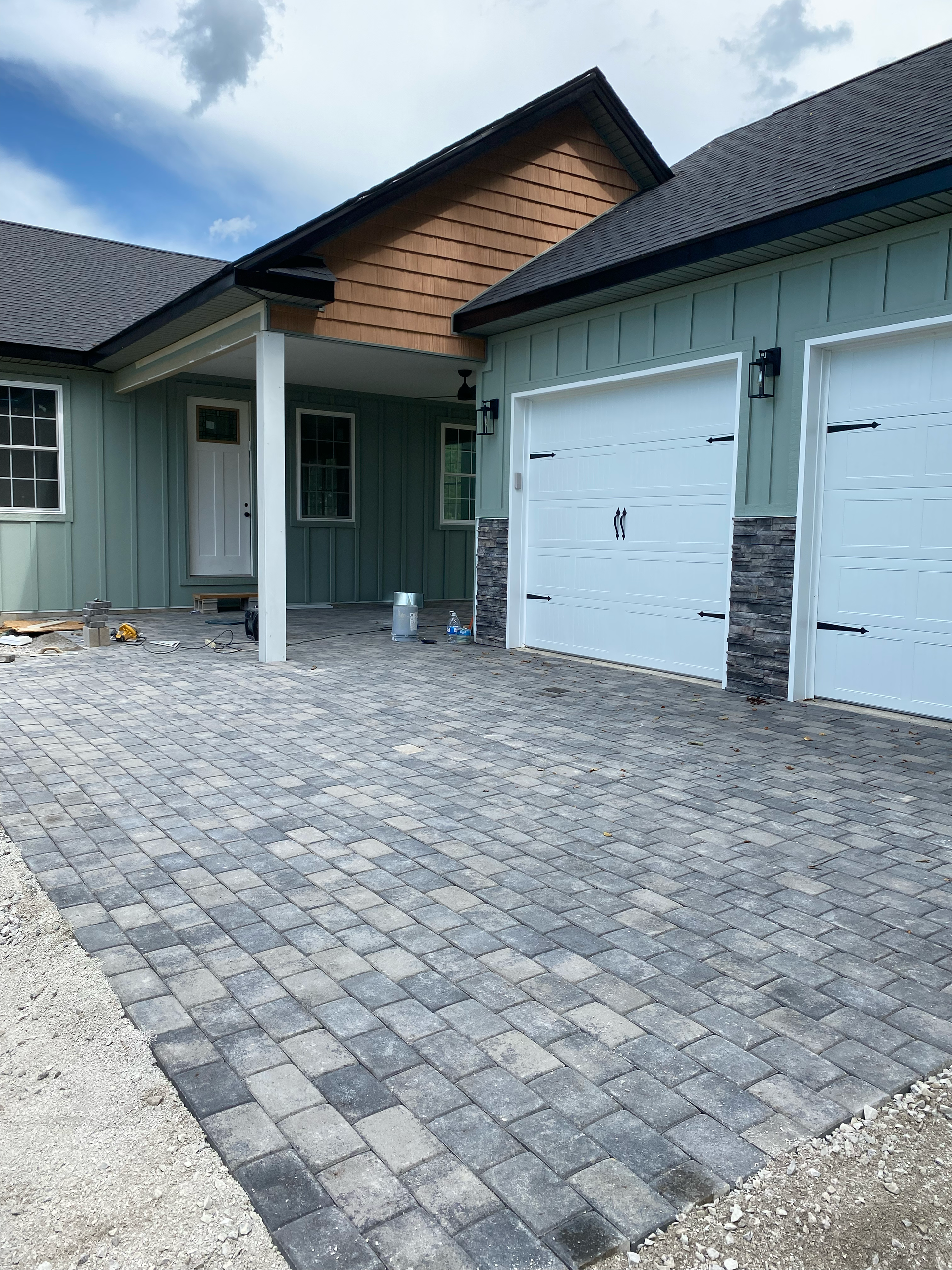 Modern house exterior with gray paver driveway, white garage doors, and covered front entry