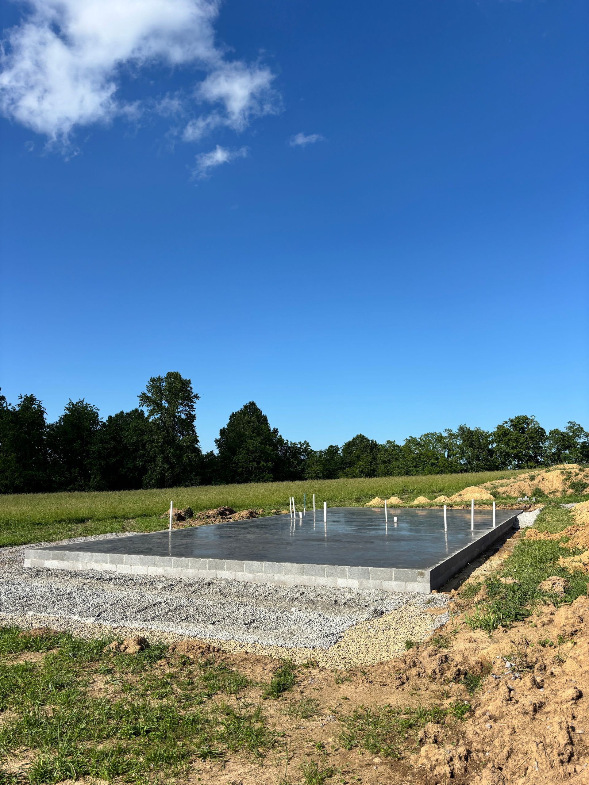 Concrete foundation slab under construction on a gravel site with a blue sky and trees in the background