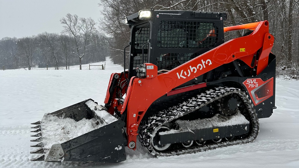 Orange skid steer clearing snow in a snowy field