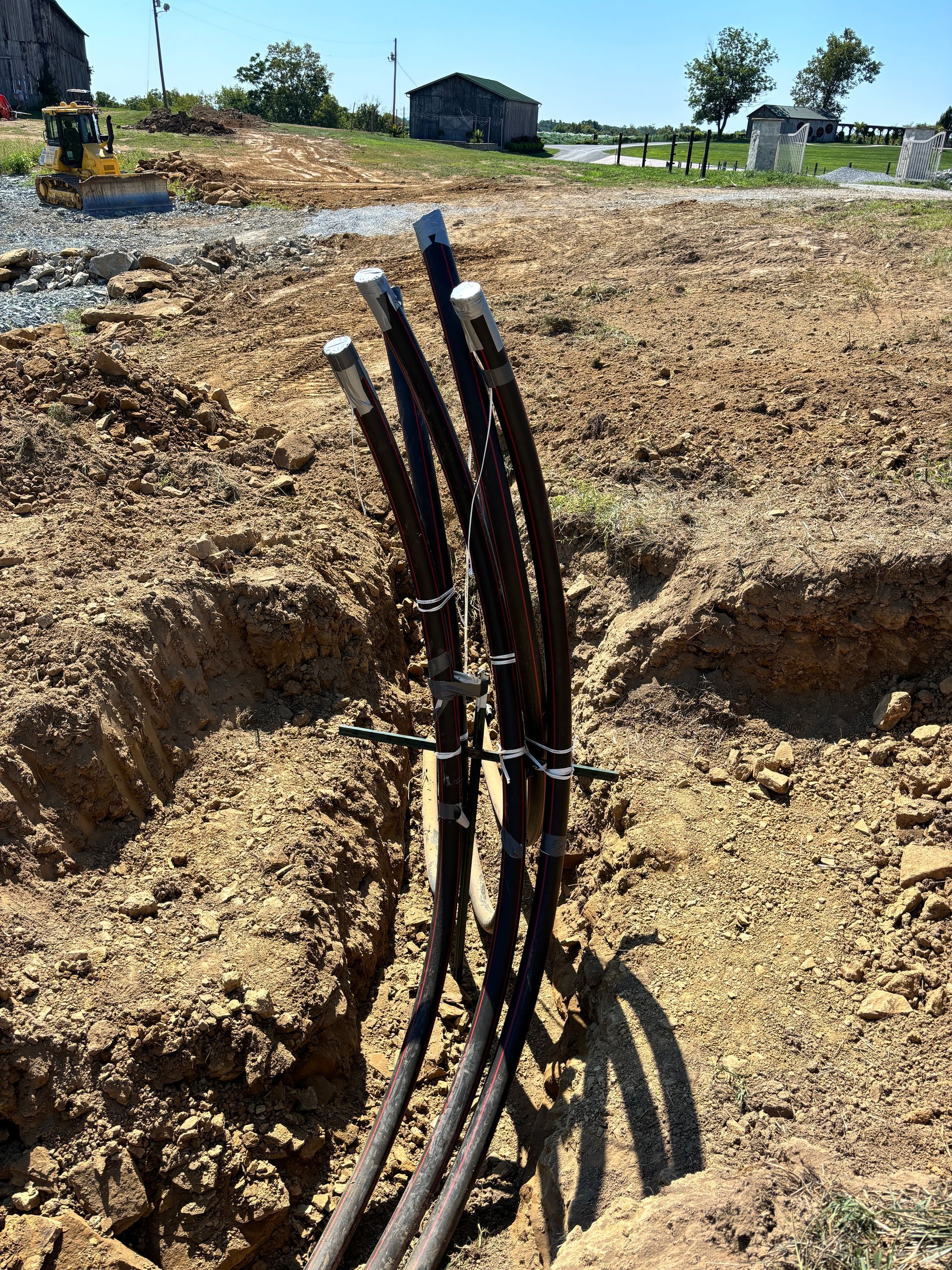 Bundle of black cables protruding from a trench in a dirt field under a clear sky