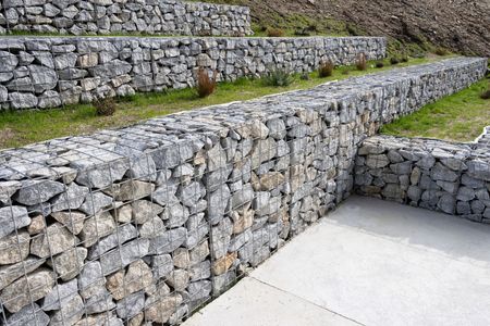 Stone retaining walls and steps in a landscaped outdoor area beside a concrete path.