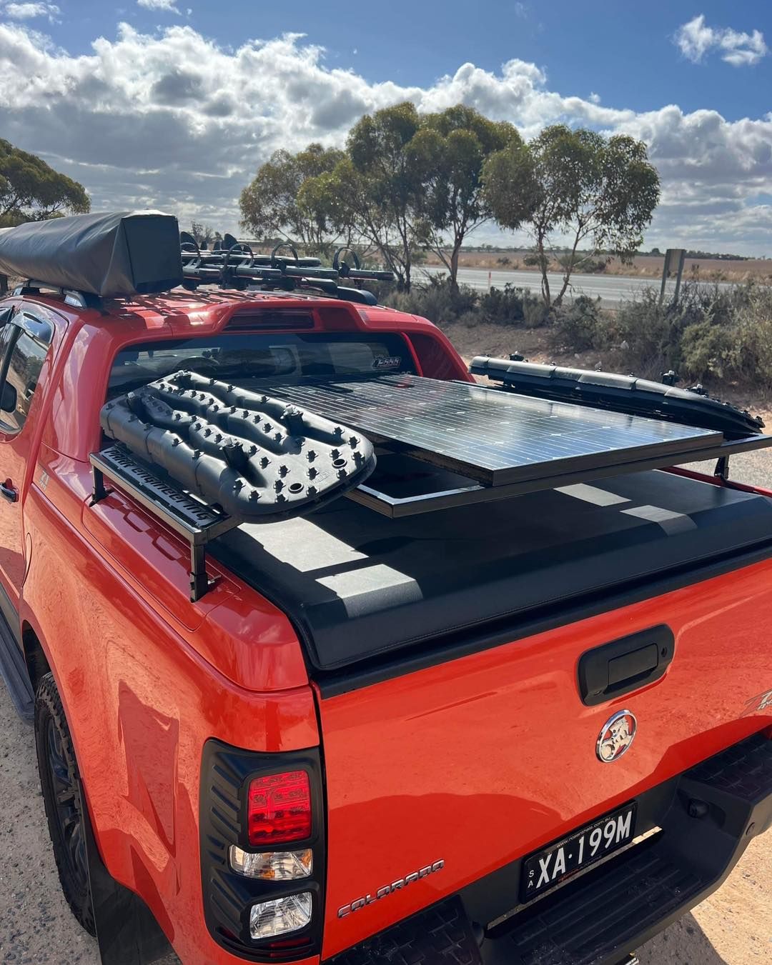 A red truck with a surfboard in the bed is parked on the side of the road.