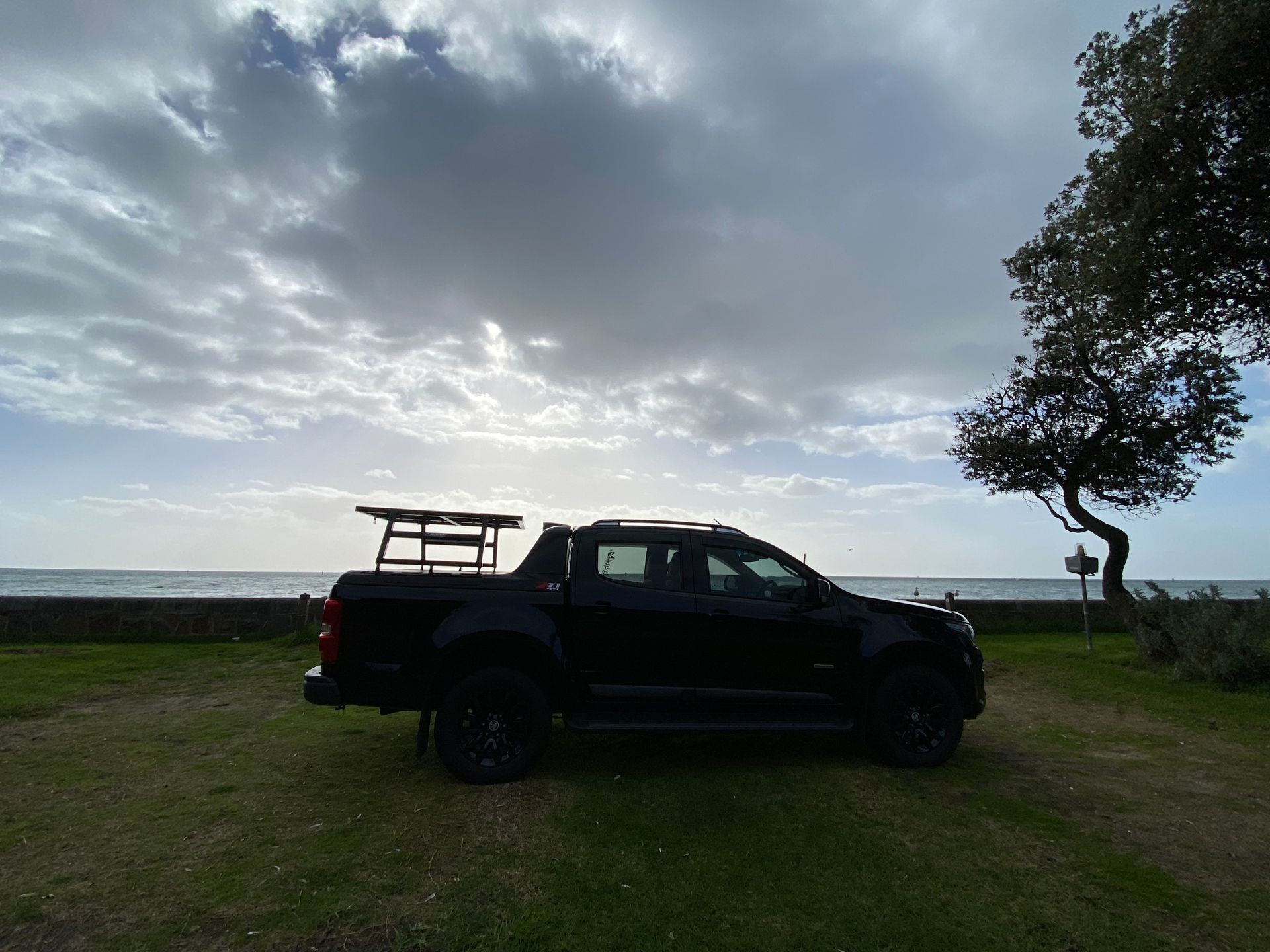 A black truck is parked in a grassy area near the ocean.