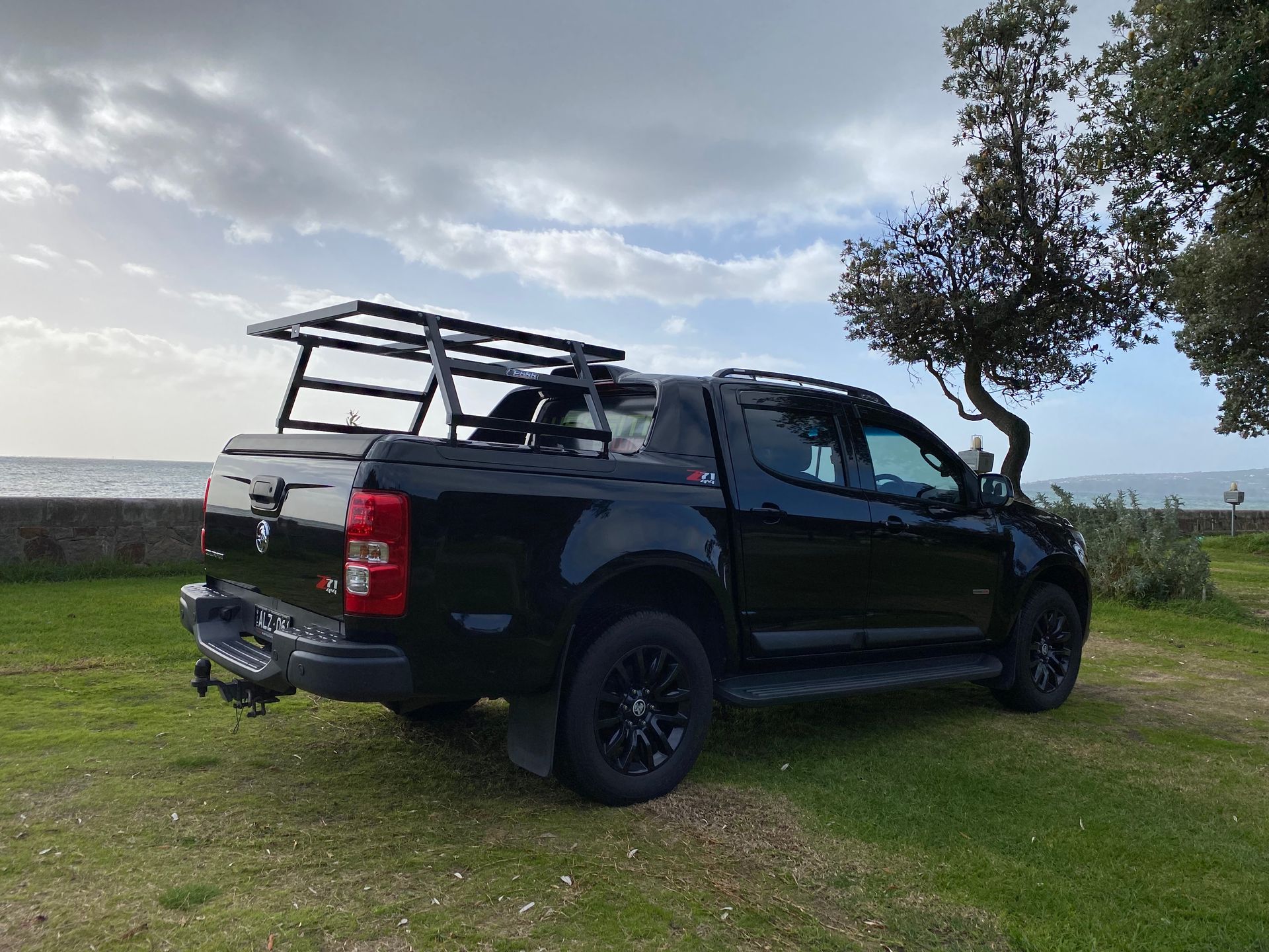 A black truck with a rack on the back is parked in a grassy field.