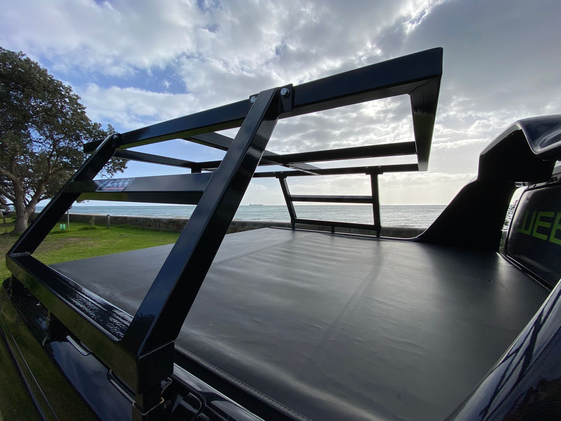 A black truck with a roof rack on it is parked in front of the ocean.
