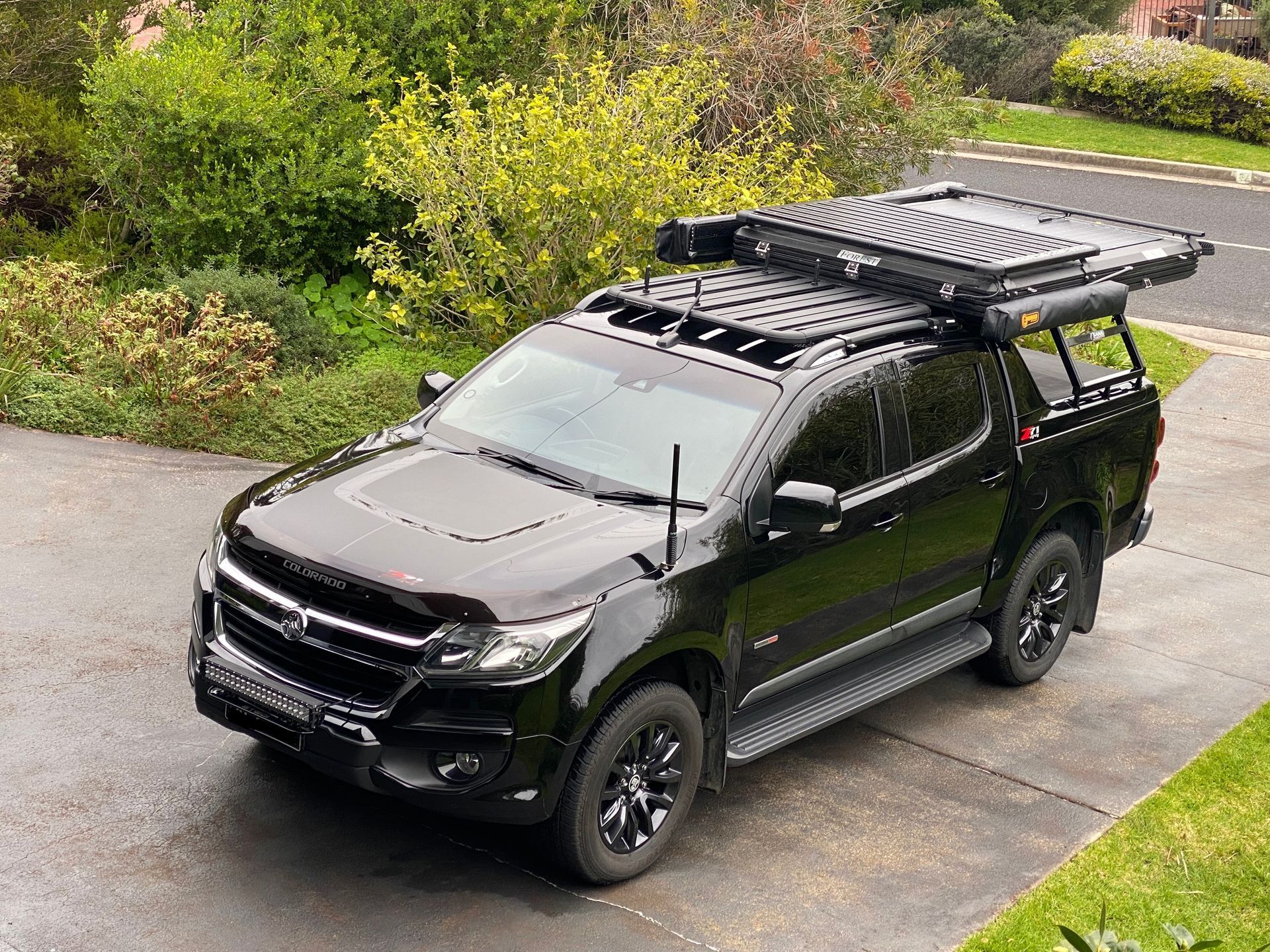 A black truck with a roof rack is parked in a driveway.