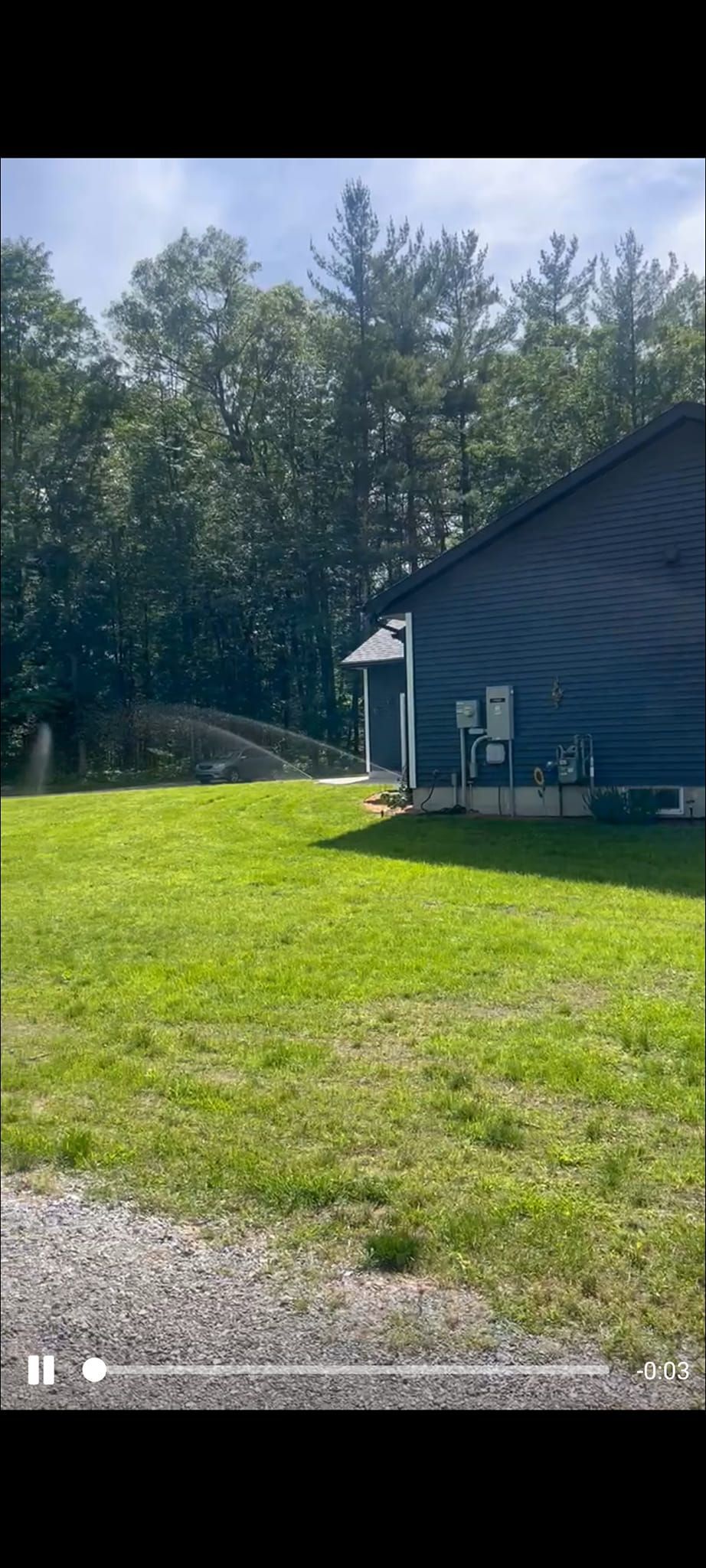 A side view of a dark blue house exterior with an attached garage, set against a green lawn and a forest background.