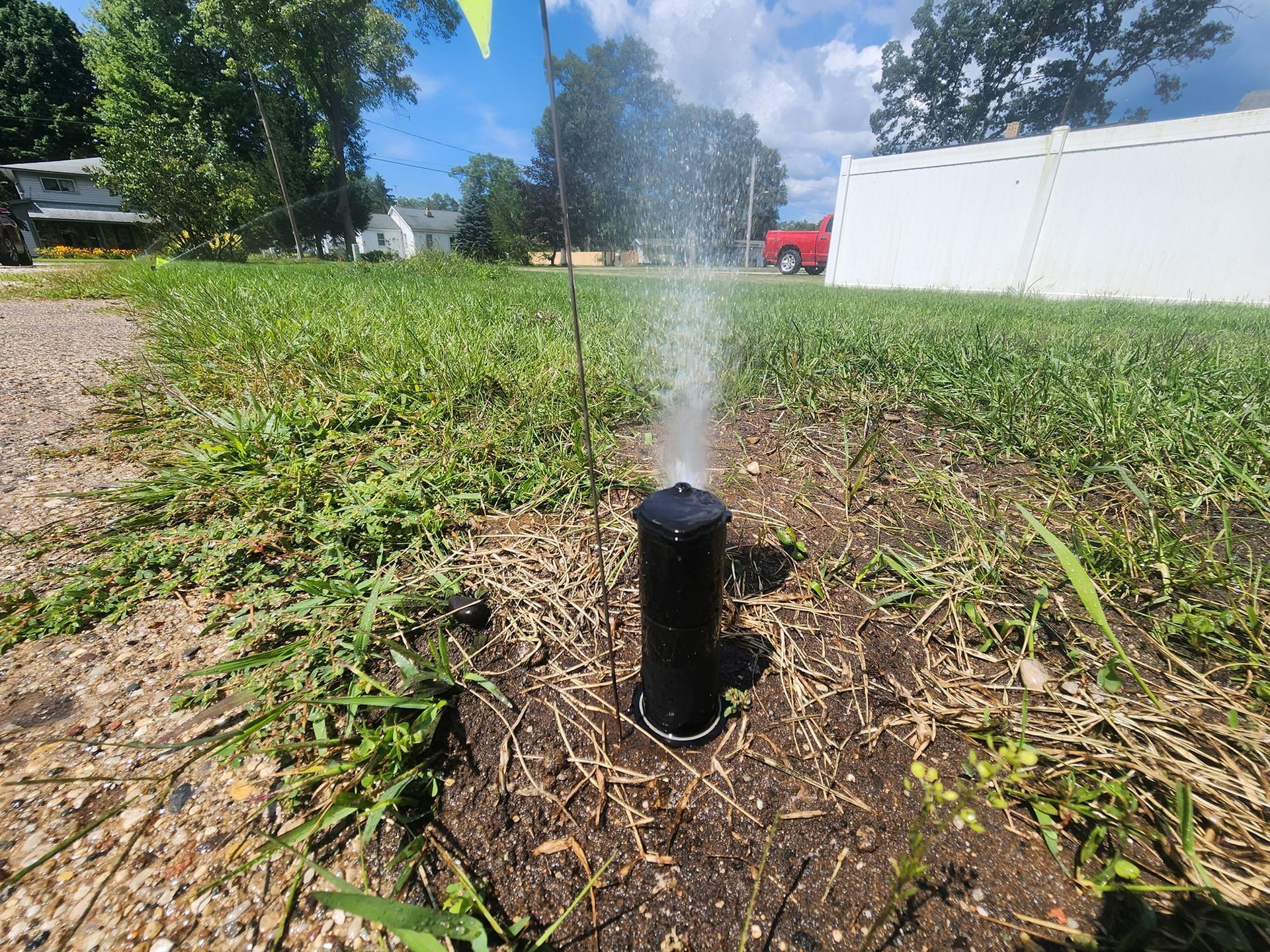 A black lawn sprinkler head in the ground spraying a vertical stream of water onto a patch of grass.