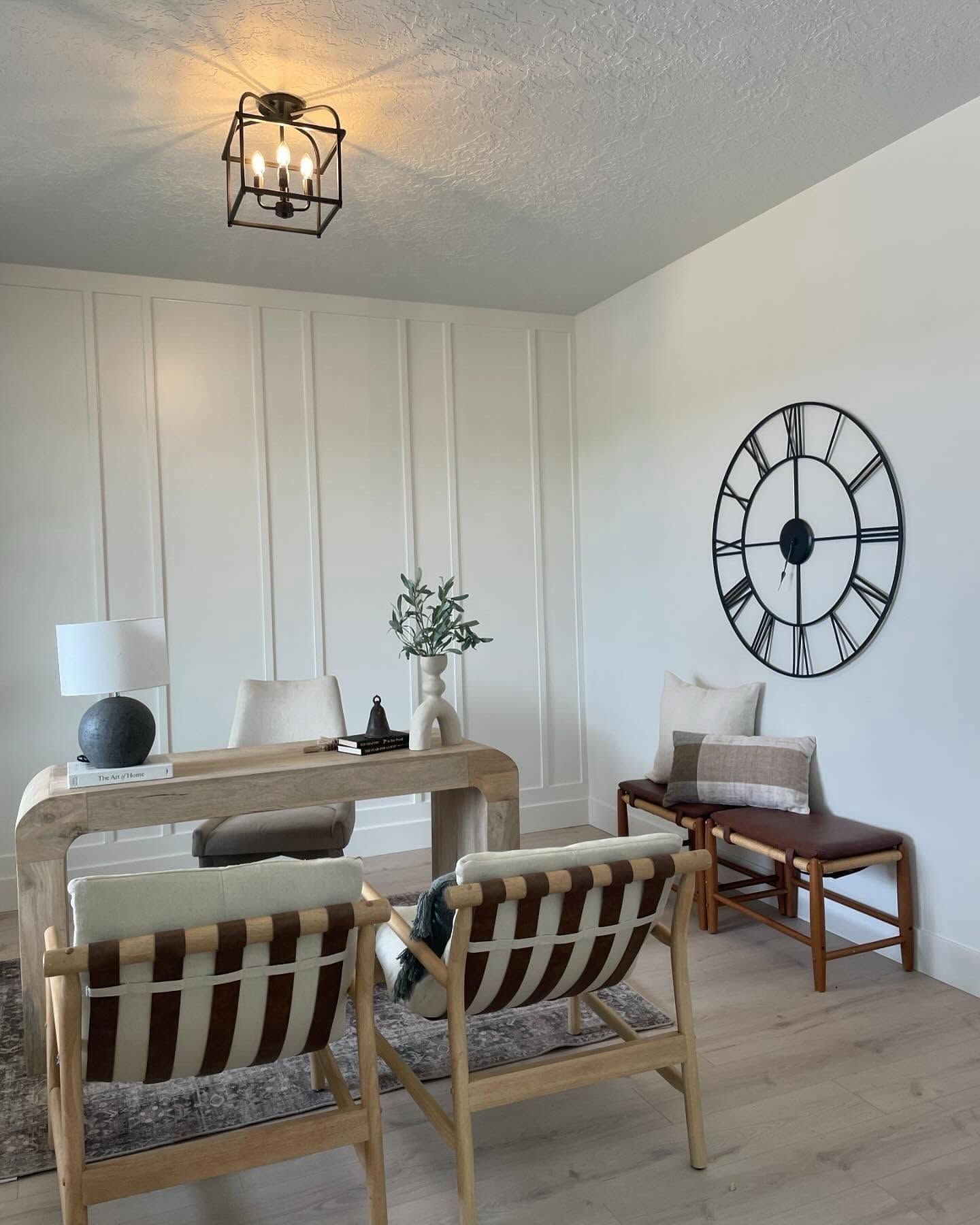 Bright dining room with wooden table, cane chairs, wall clock, bench, and geometric ceiling light.