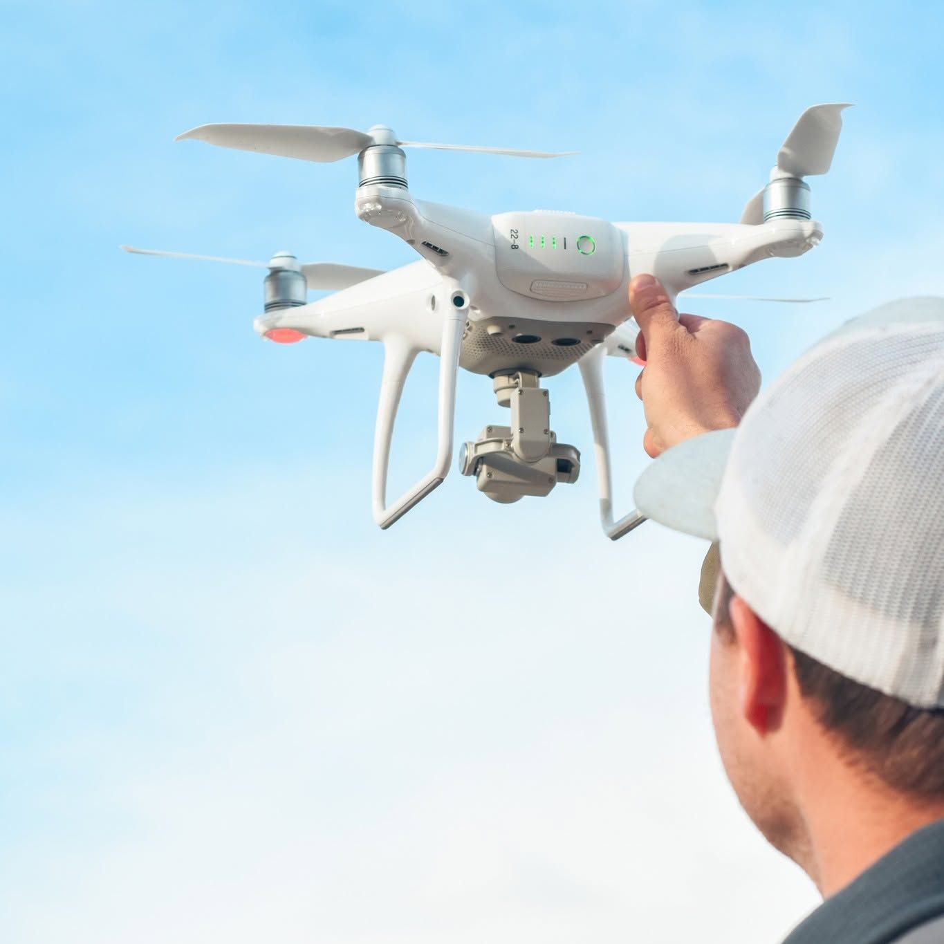 Person launching a white drone outdoors against a blue sky
