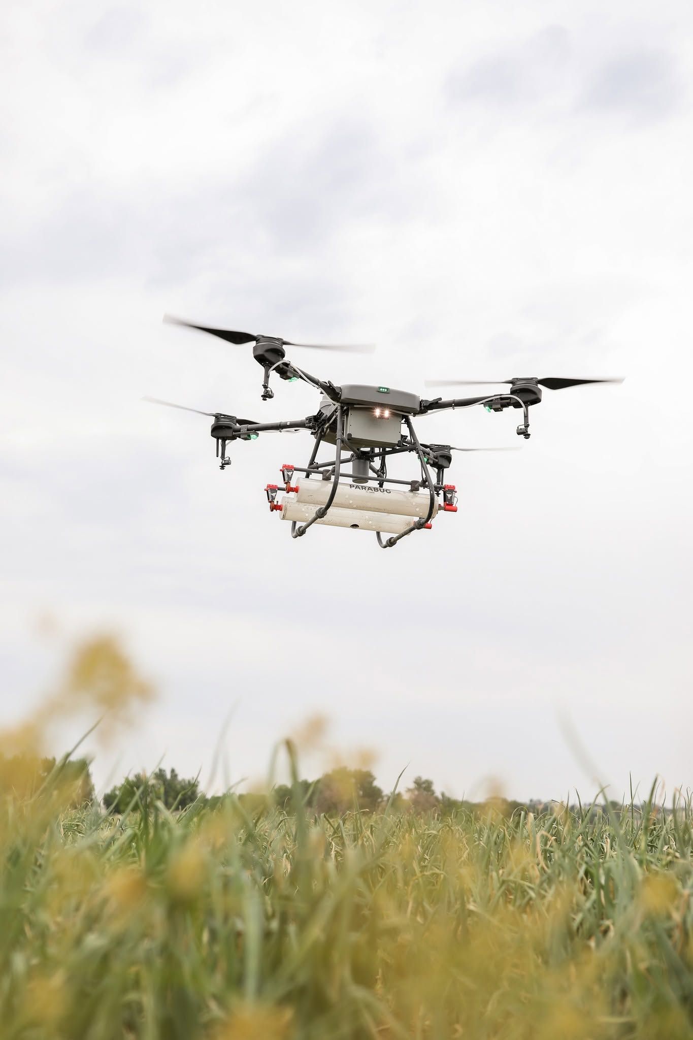 Drone hovering low over a grassy field against a cloudy sky