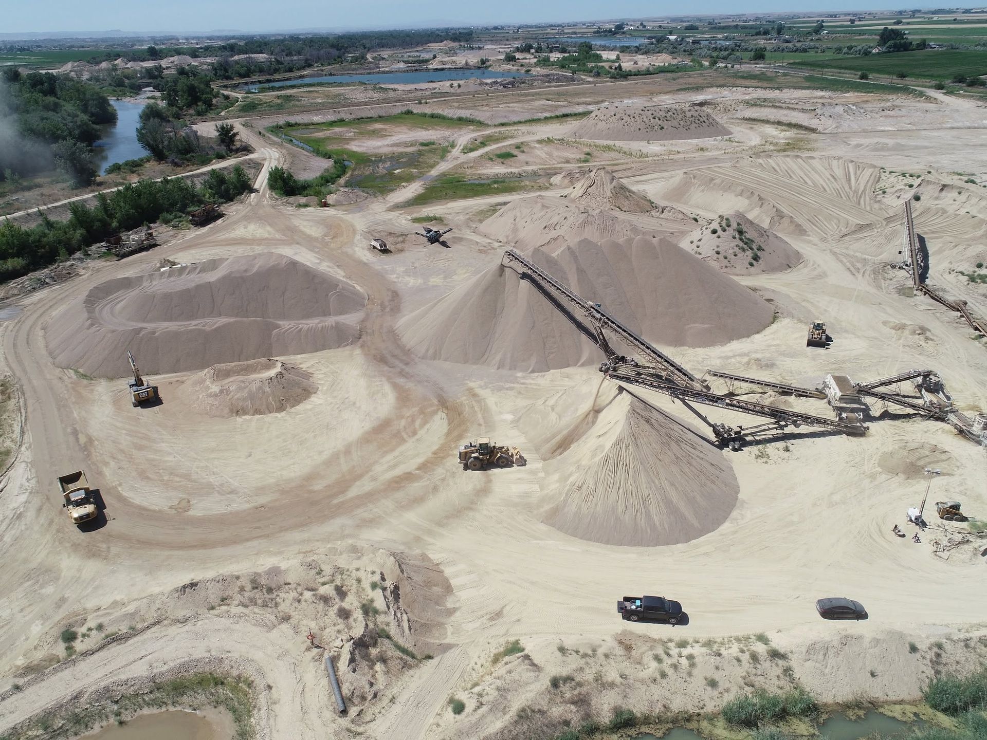 Aerial view of a sandy quarry with large gravel mounds and several dump trucks