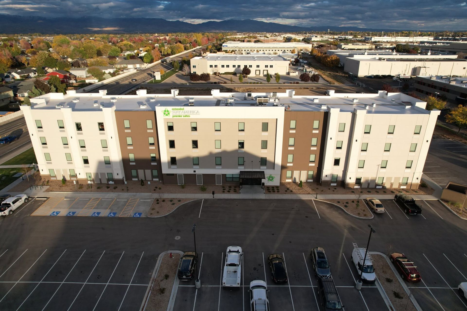 Aerial view of a beige and brown apartment building with a parking lot in front at dusk.