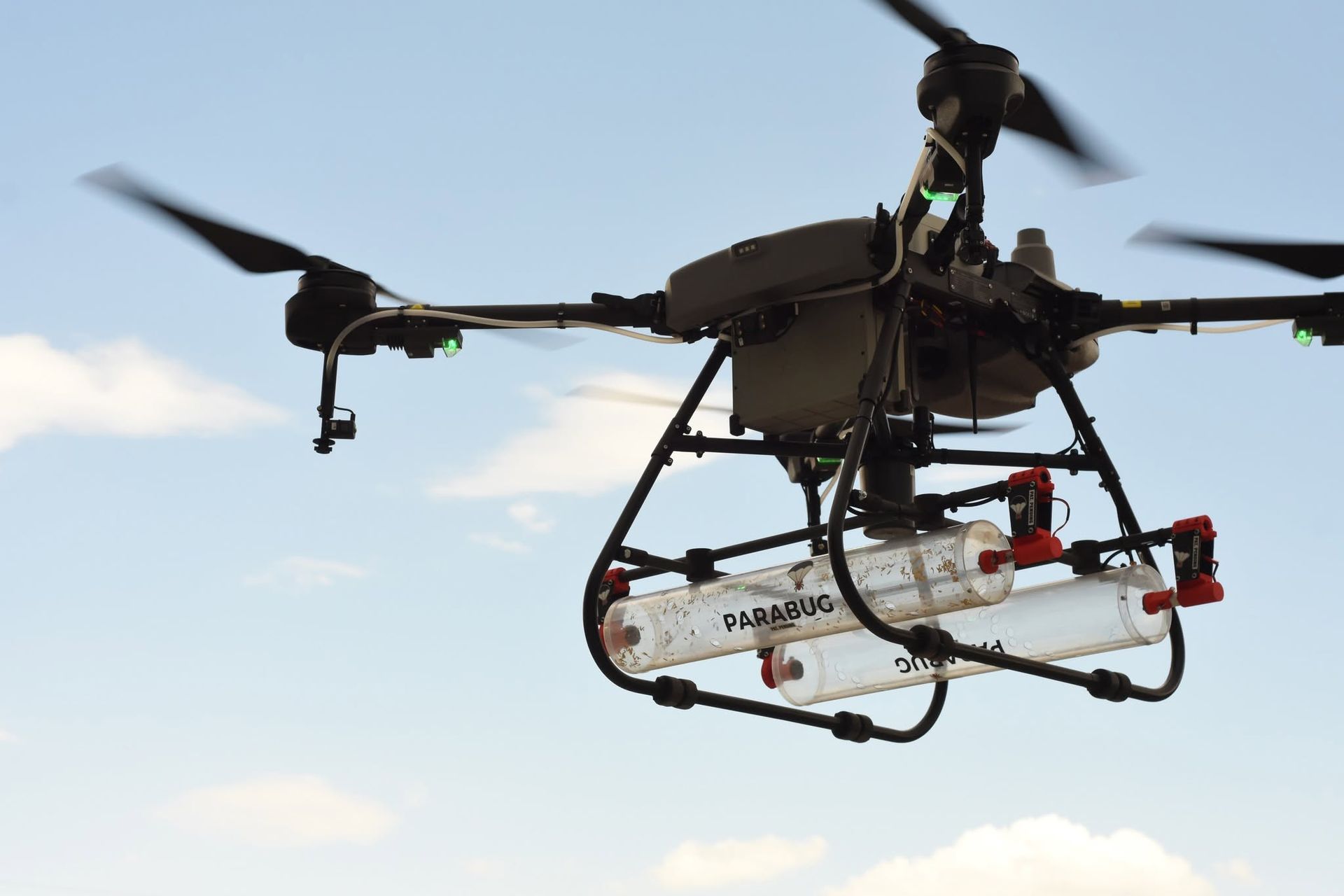 Black drone helicopter with landing gear and rotors flying against a blue sky.