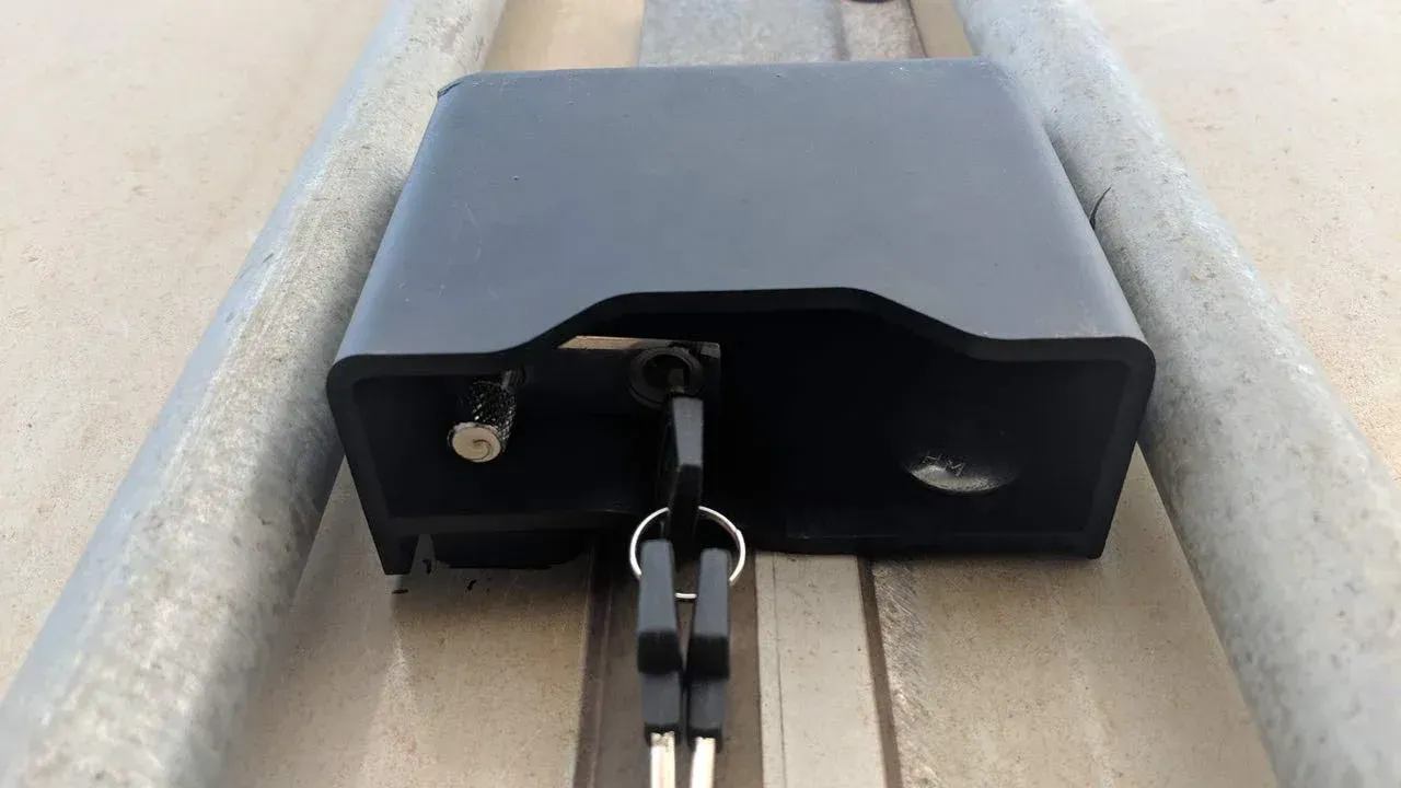 a black padlock with a key attached to it is sitting on a railing shipping container lockbox.