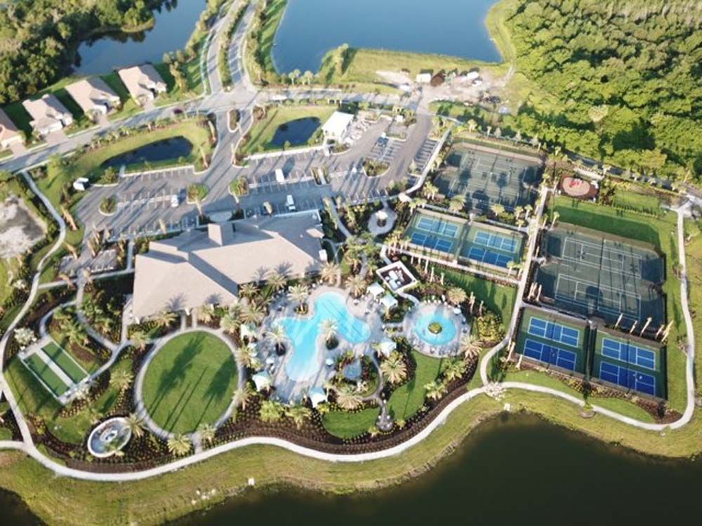 Aerial view of a water park with pools, slides, tennis courts, and nearby buildings by a lake