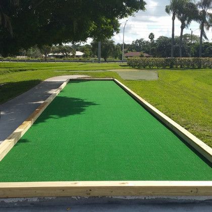 Green mini-golf putting lane bordered by wooden rails in a sunny park