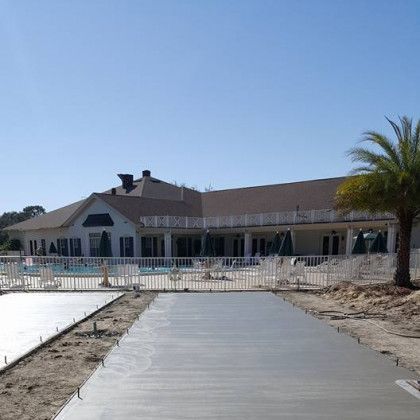 White beachfront house with a pool and palm tree beside a newly poured concrete walkway under a clear blue sky