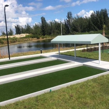 Outdoor miniature golf course with green putting lanes, white borders, and a small covered shelter by a pond.