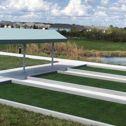Covered outdoor seating area with a green roof, set beside a grassy field under a clear sky.