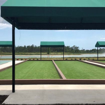 Covered lawn bowling green with green canopies and a lake in the background