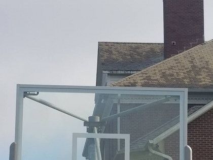 Metal rooftop structure with a small wind turbine beside a house chimney under a gray sky