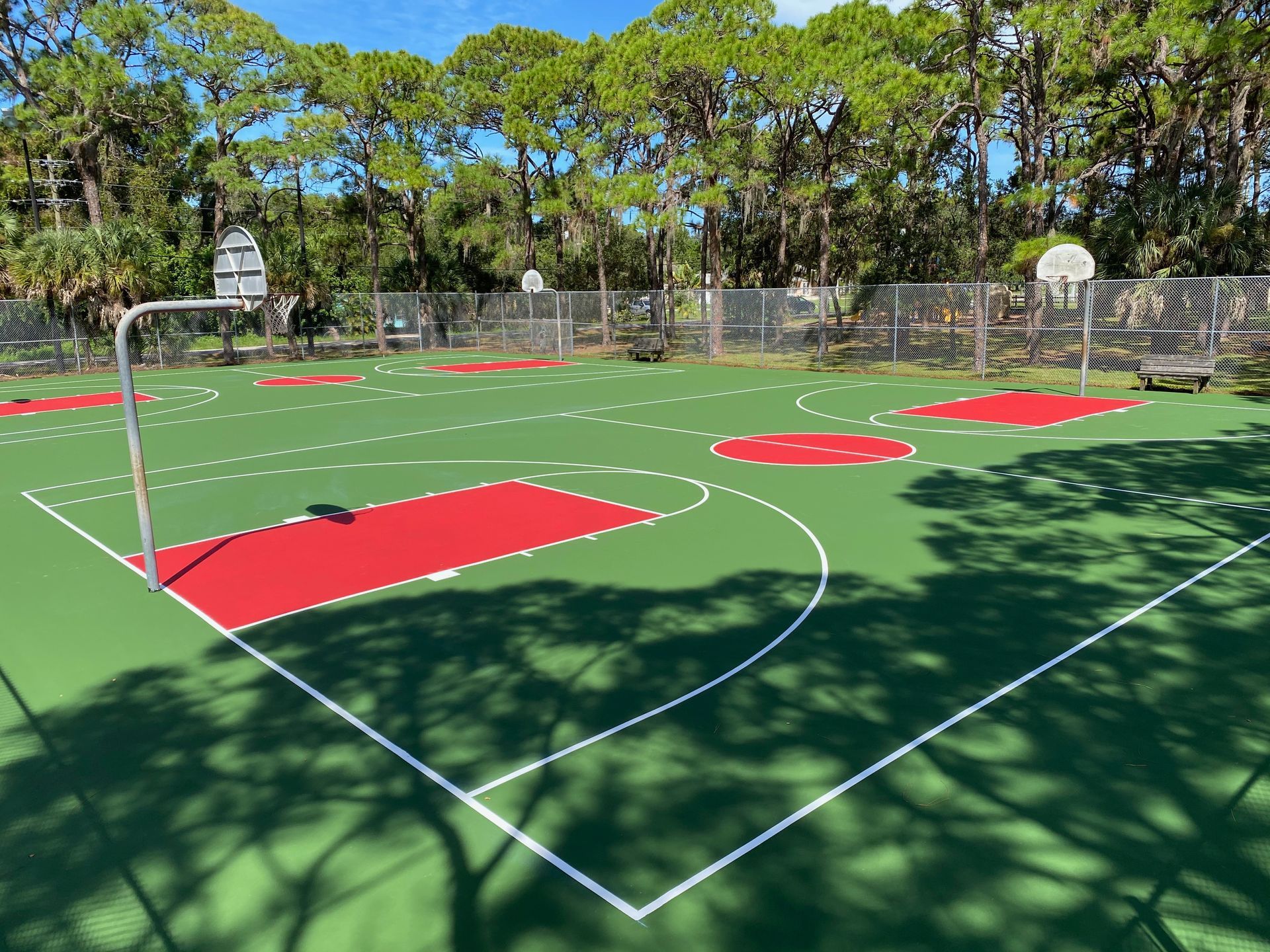 Outdoor sports court with red painted zones, white boundary lines, and trees in the background