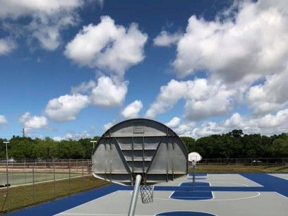 Outdoor basketball court with blue pavement and two hoops under a cloudy sky